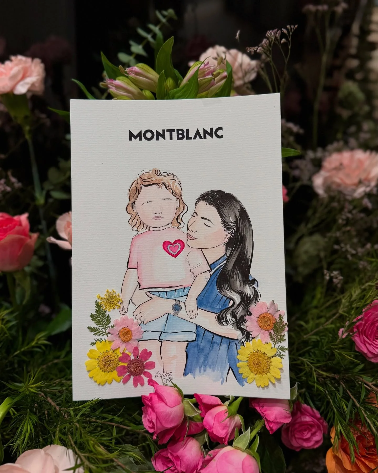 A drawing of two women, one with curly hair and a child, surrounded by colorful flowers, with the brand name 'Montblanc' at the top.