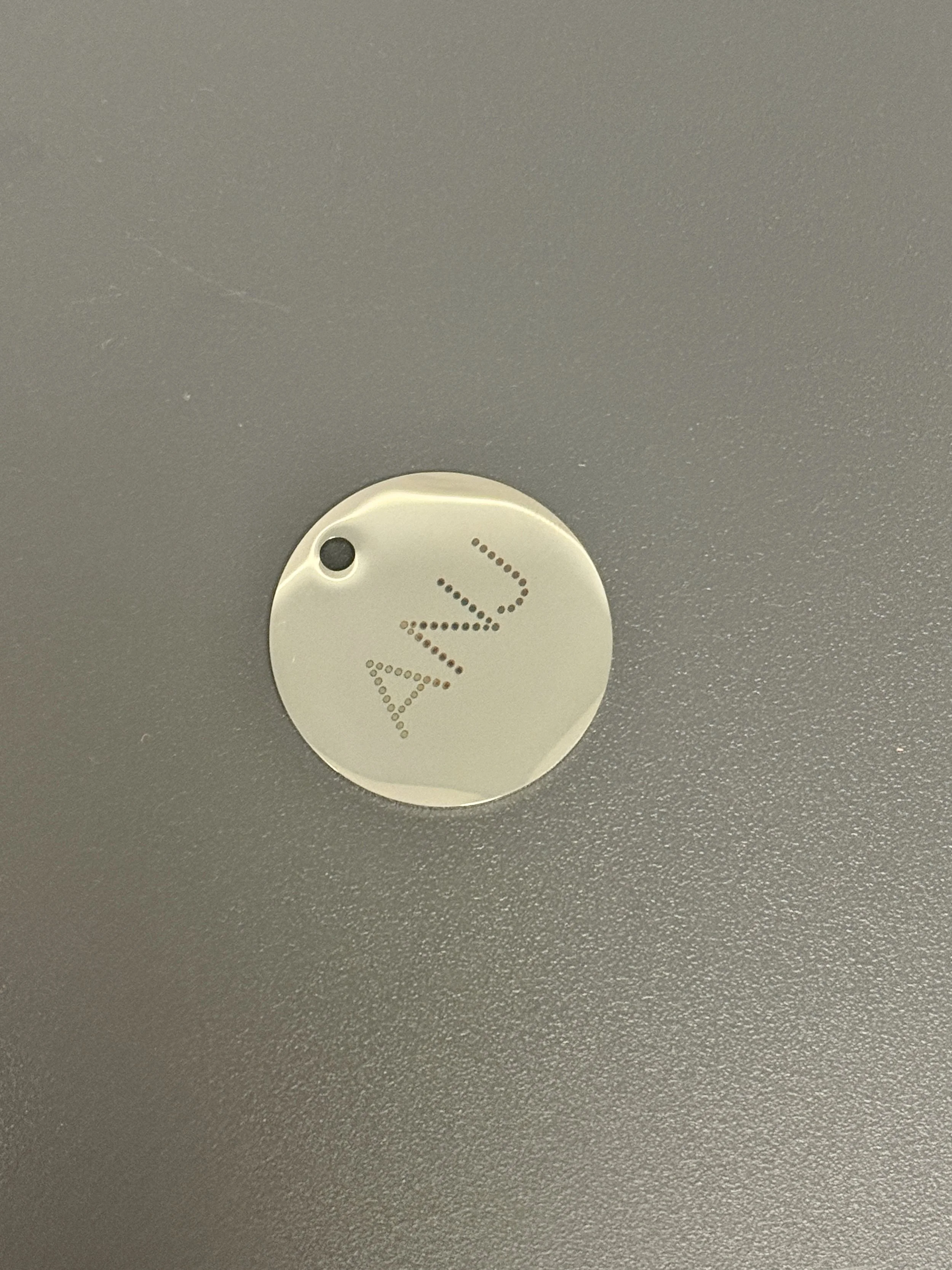 Close-up image of a white circular eco-friendly tag with the word "dva" written in dotted letters, placed on a dark gray textured surface.