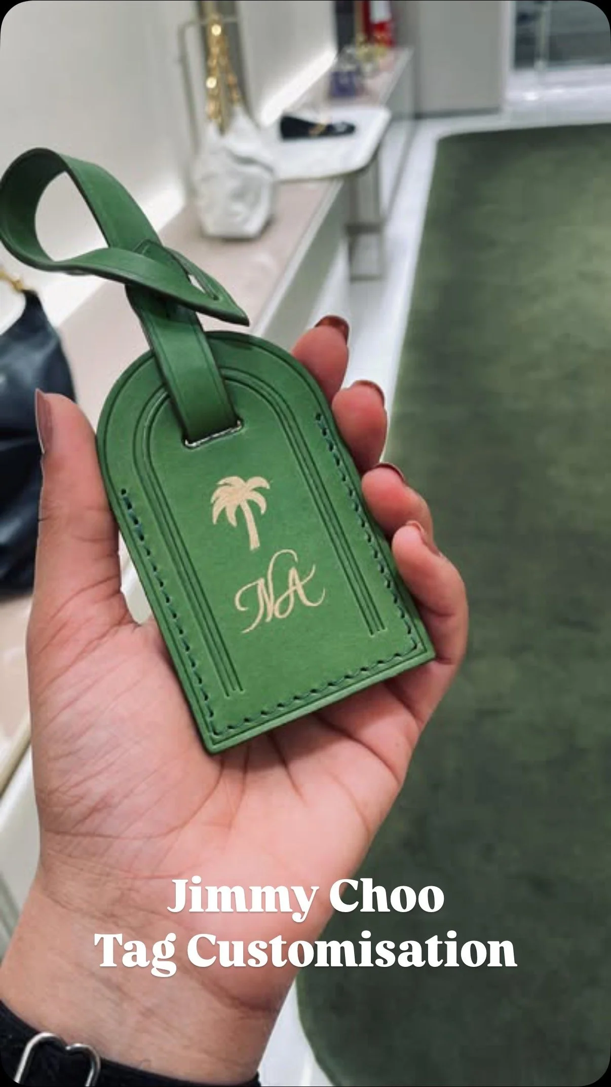 A hand holding a green Jimmy Choo tag with a palm tree and the initials 'MC' on it, in a retail setting with shelves and other items in the background.