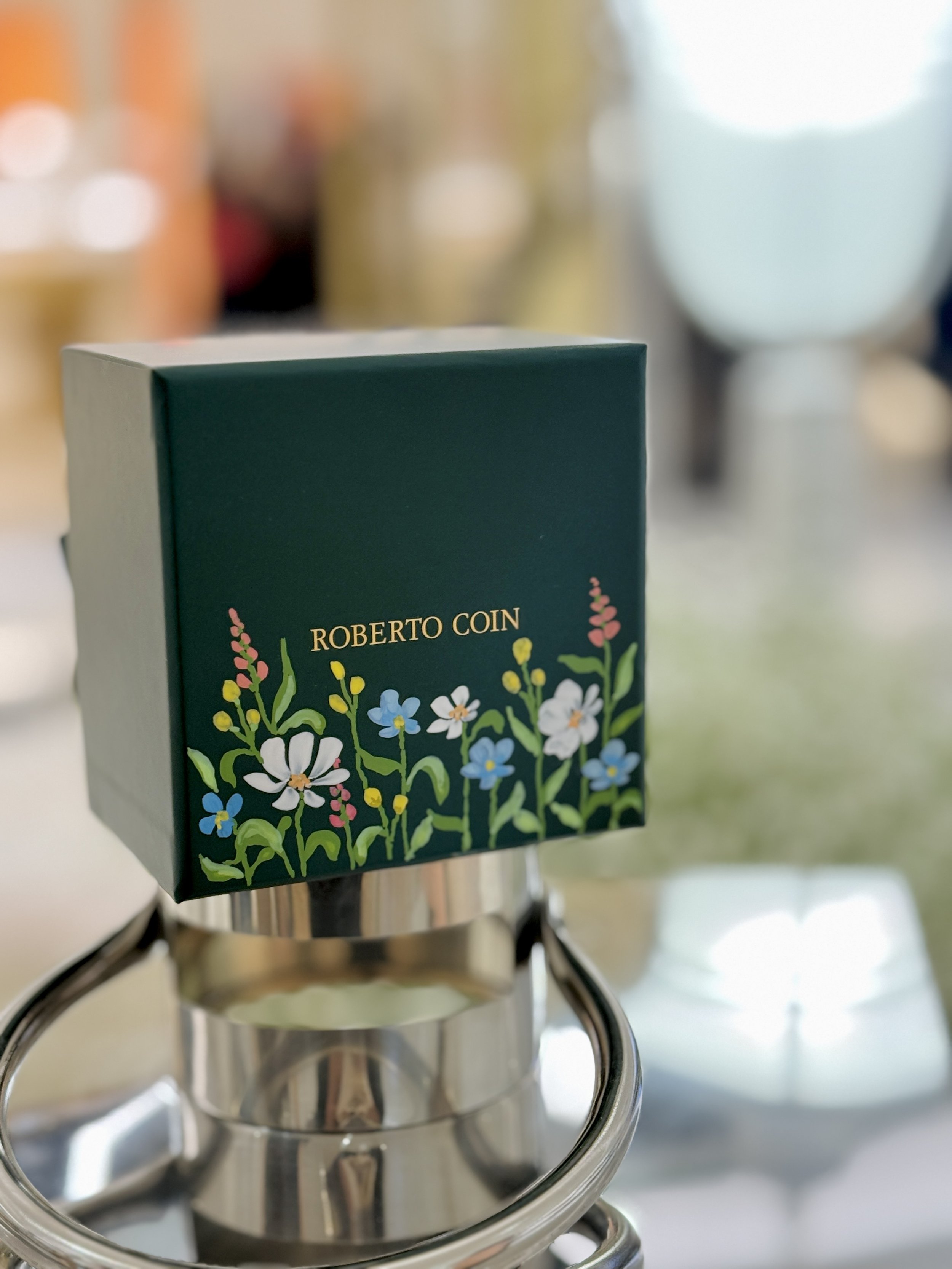 A box with floral design and the words "Roberto Coin" resting on the rim of a glass jar on a stove.