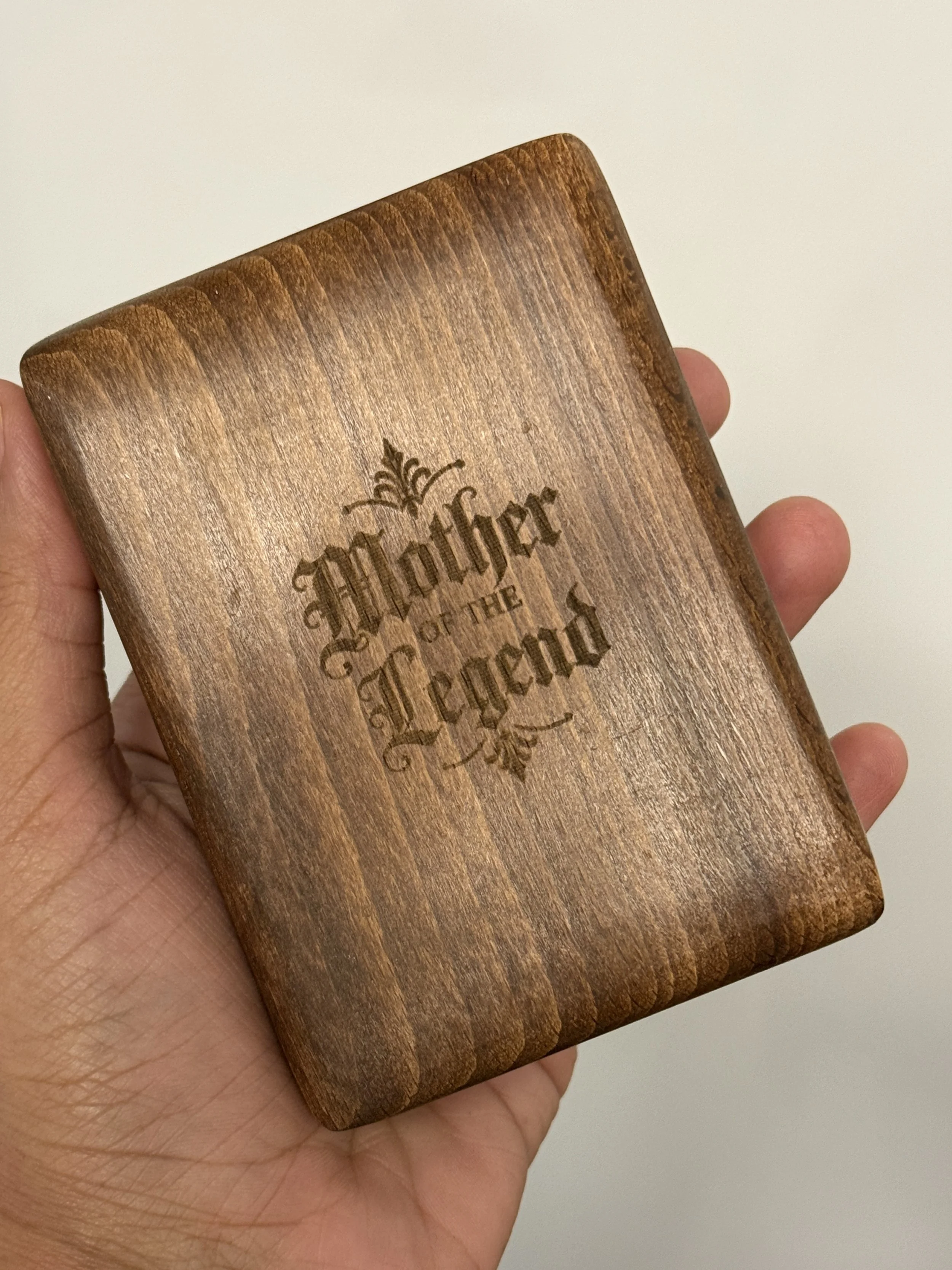 A person holding a wooden card with engraved text that reads "Solfinder" and some decorative elements.