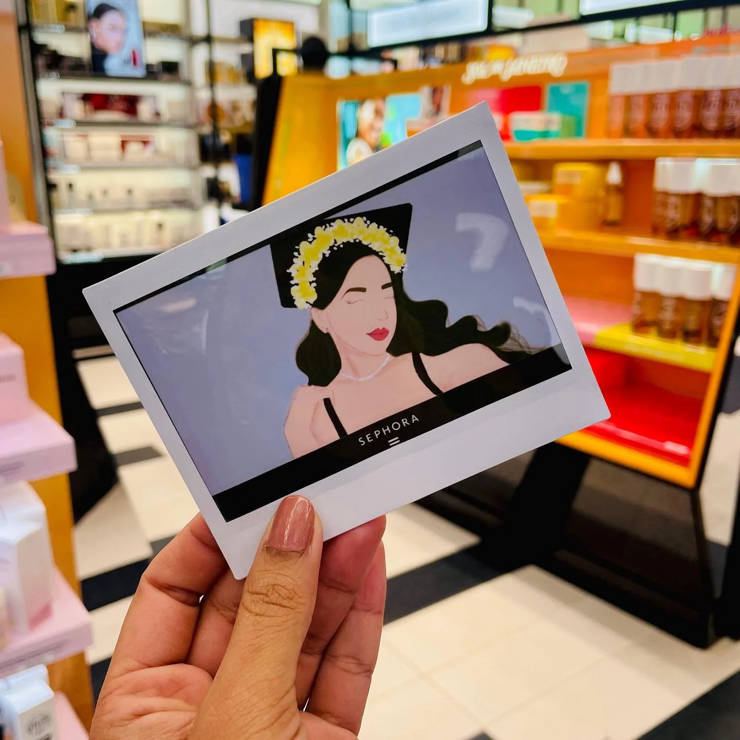 A person holding a Sephora gift card with an illustration of a woman wearing a graduation cap and a flower crown, winking, and smiling.