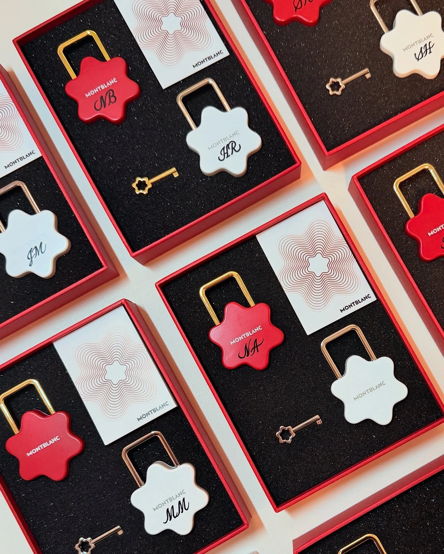 Several Montblanc keychains in red and white, each in a red box with black foam inserts. The keychains have the Montblanc logo and either 'NA' or 'MR' written on them.