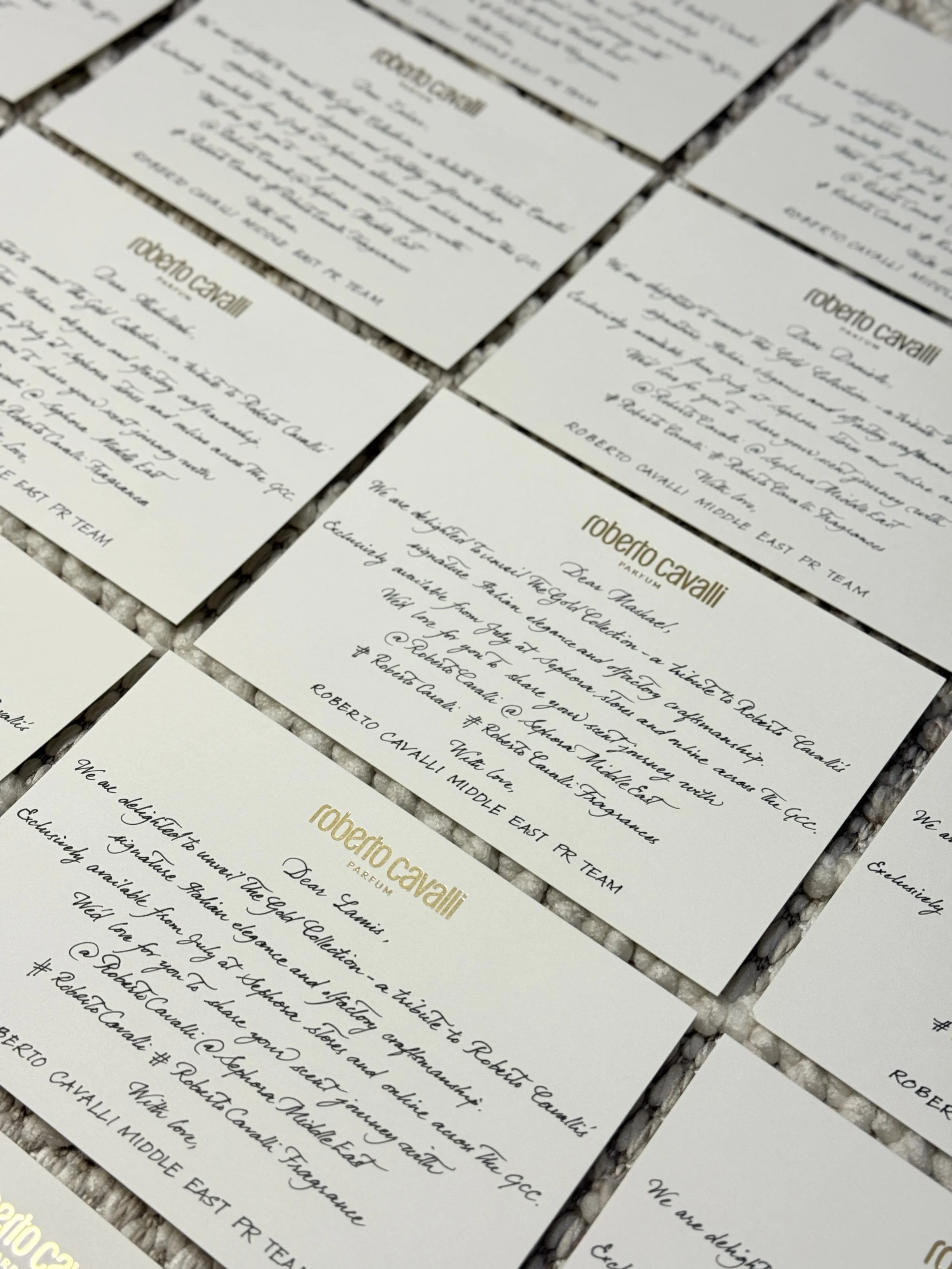 Several white business cards with handwritten text and gold lettering display on a textured surface.