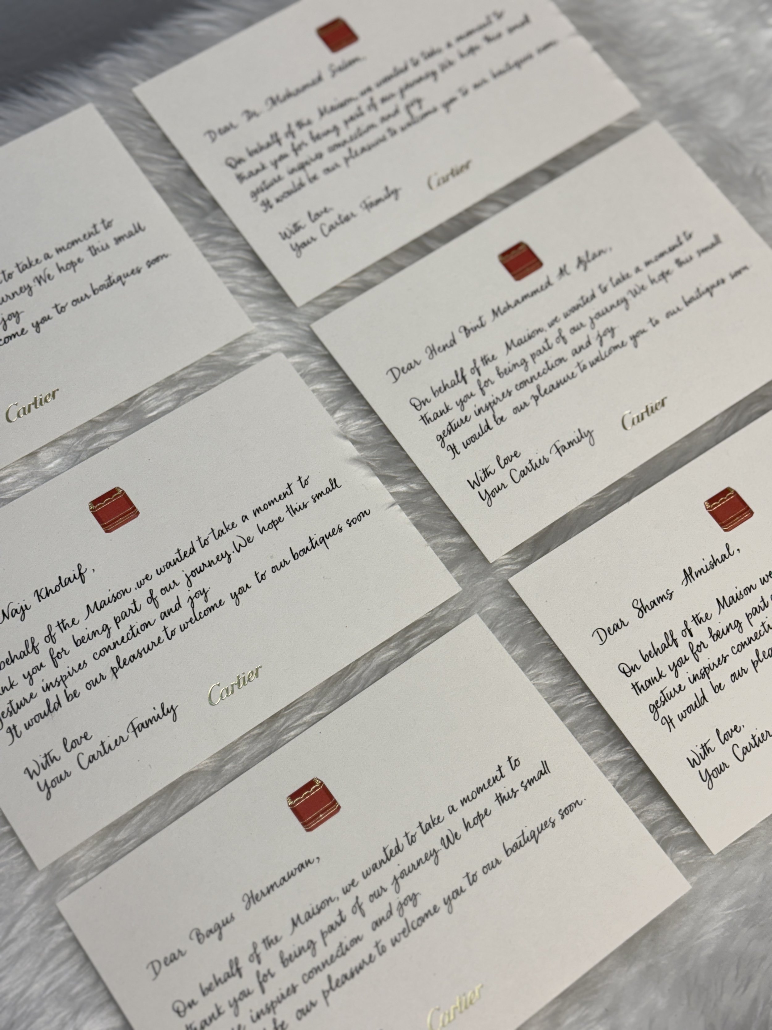 Close-up of several handwritten thank you notes on white paper with Cartier logos, lying on a textured surface.