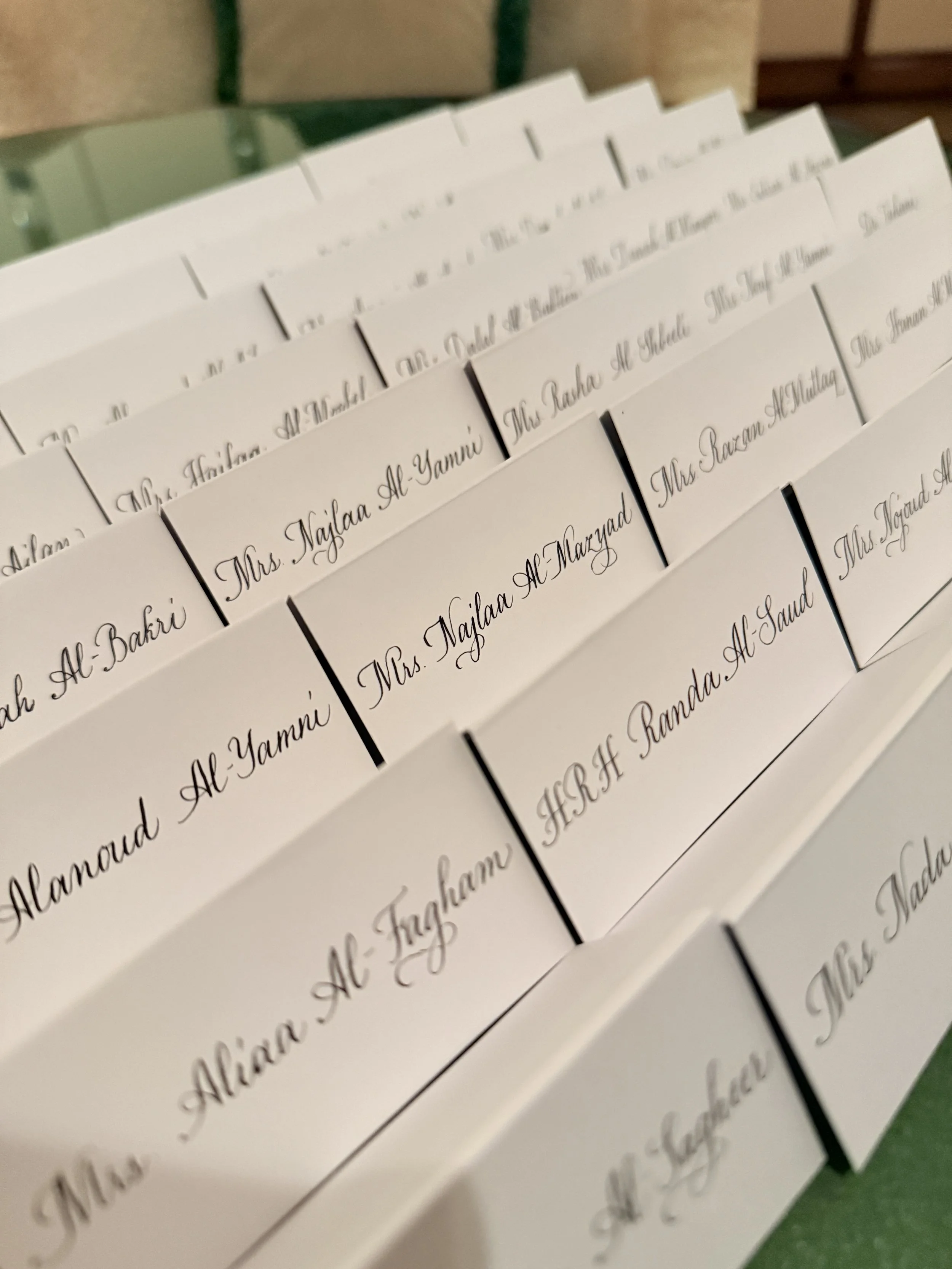 Close-up of white name cards with elegant cursive black font, arranged in a fan shape on a green surface.