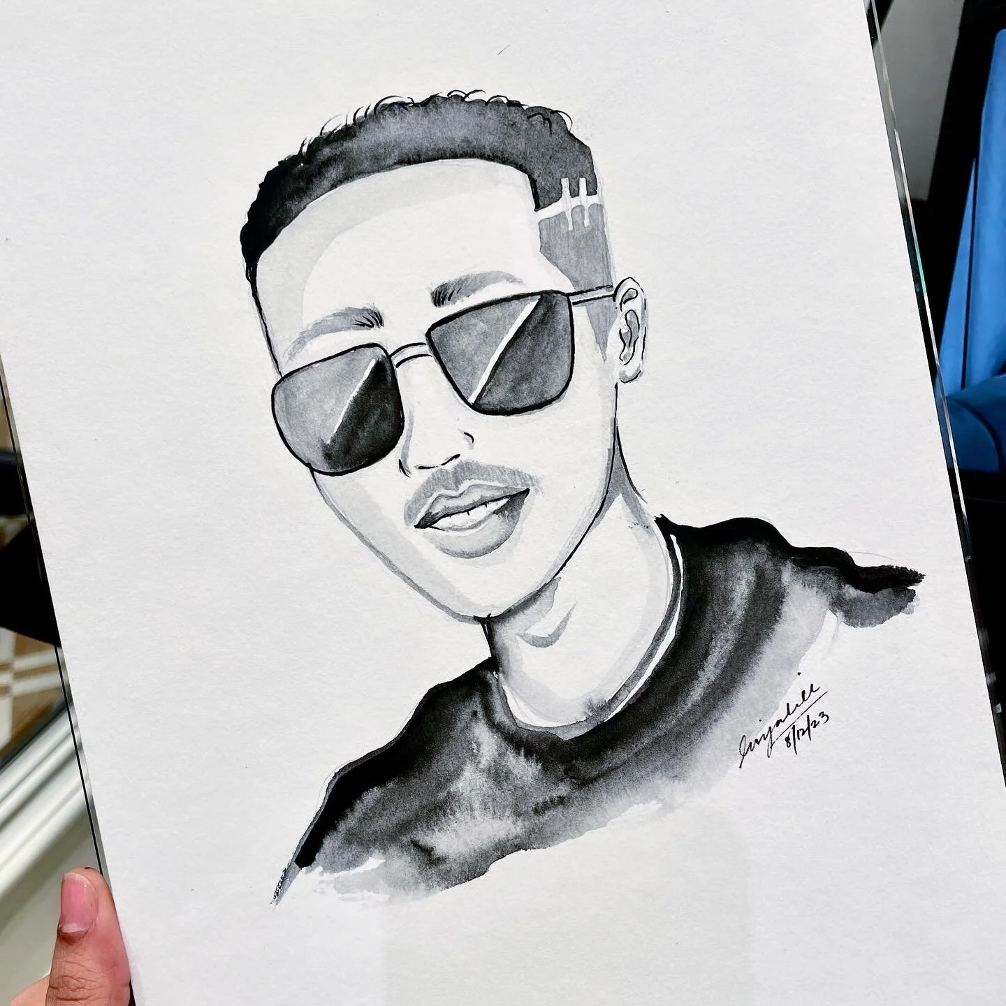 Black and white watercolor portrait of a person wearing sunglasses and a t-shirt, with short hair and a slight smile.