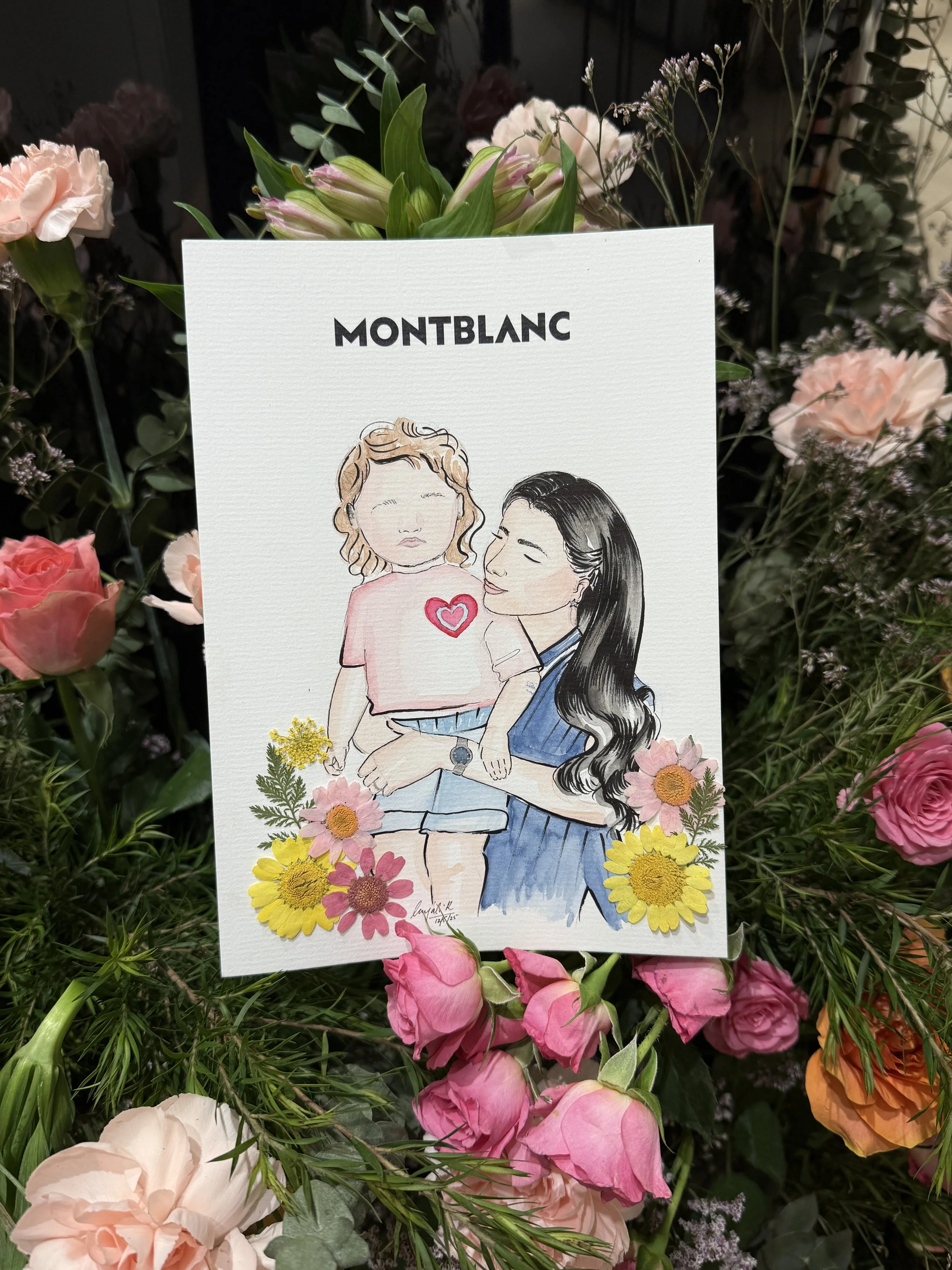 A greeting card with a hand-drawn illustration of a woman and a girl surrounded by pink, yellow, and orange flowers, placed on a bed of mixed flowers.