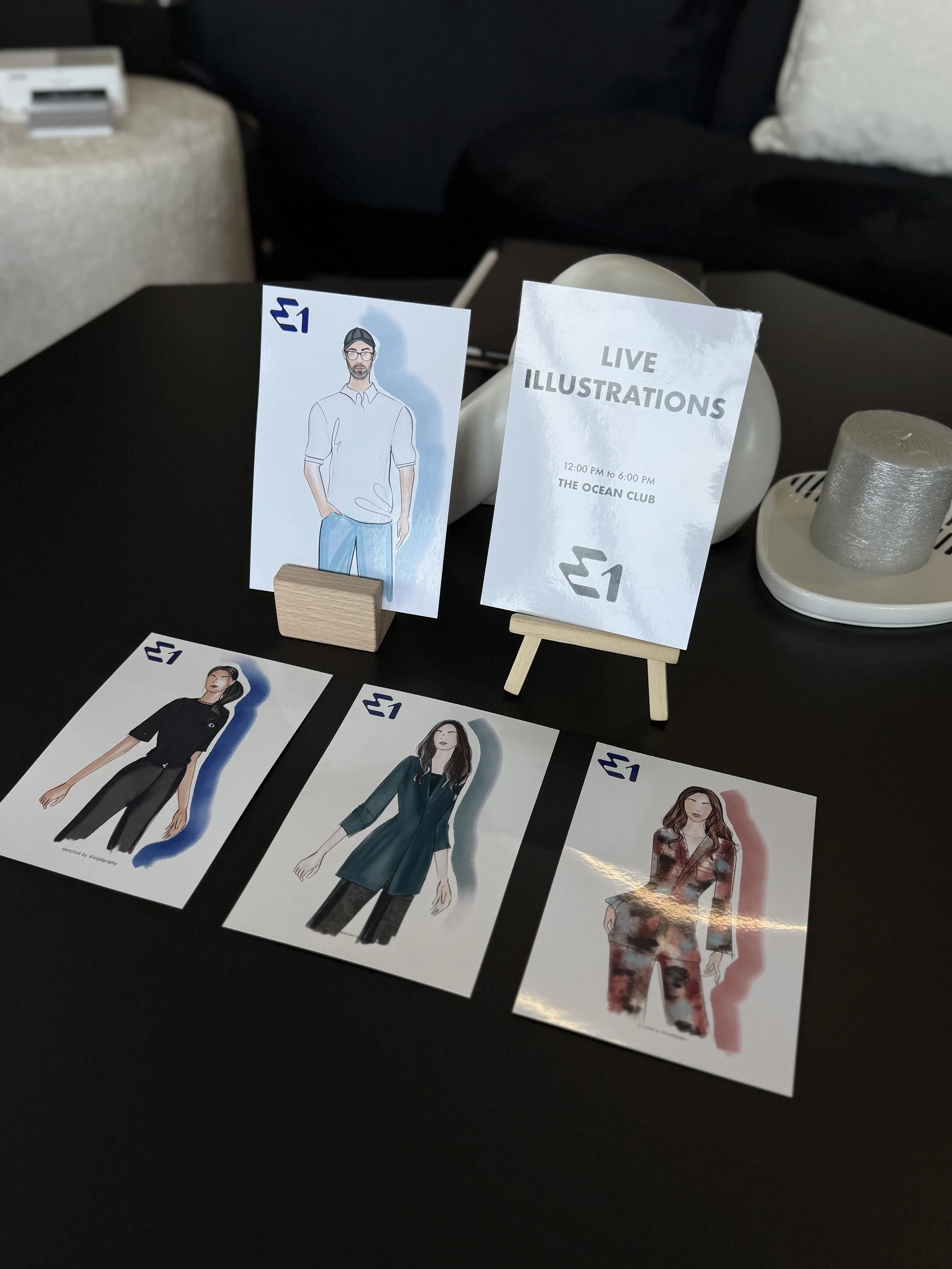 Table displays illustrated fashion models, some with watercolor effects, alongside promotional signs for live fashion illustrations event at The Ocean Club from 12:00 PM to 6:00 PM.