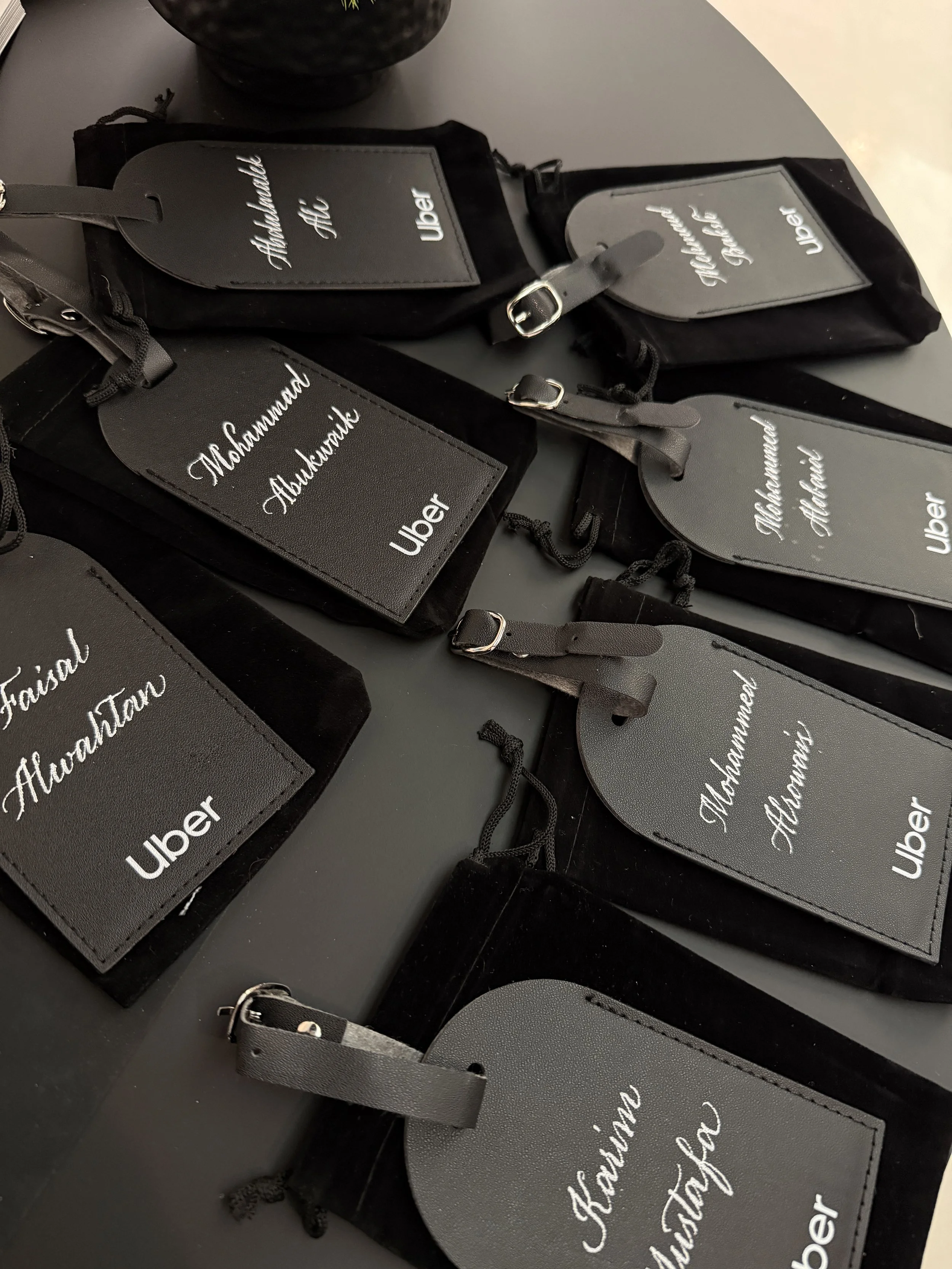 A collection of black and gray Uber luggage tags with the name 'Muhammad Alwanatik' on them, placed on a black surface.