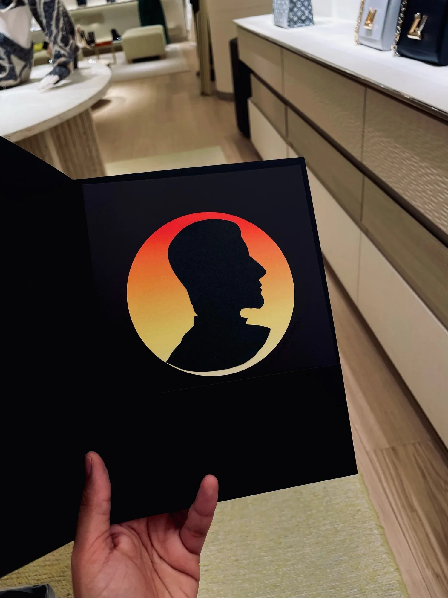 A person holding a black folder with a silhouette of a person's profile against a sunset or sunrise background.