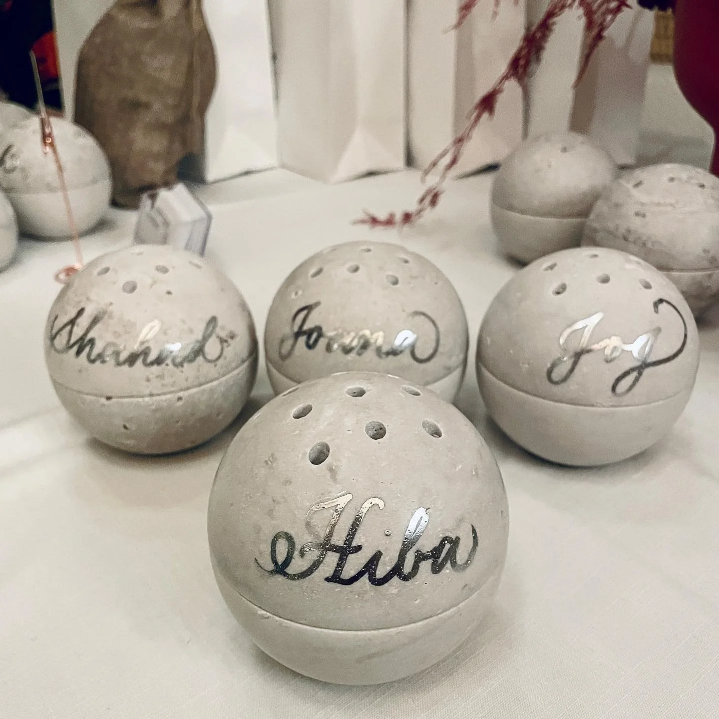 Decorative white ceramic balls with holes and handwritten words in cursive, including "Hello," "Thankful," "Journ," and "Joy," arranged on a table.