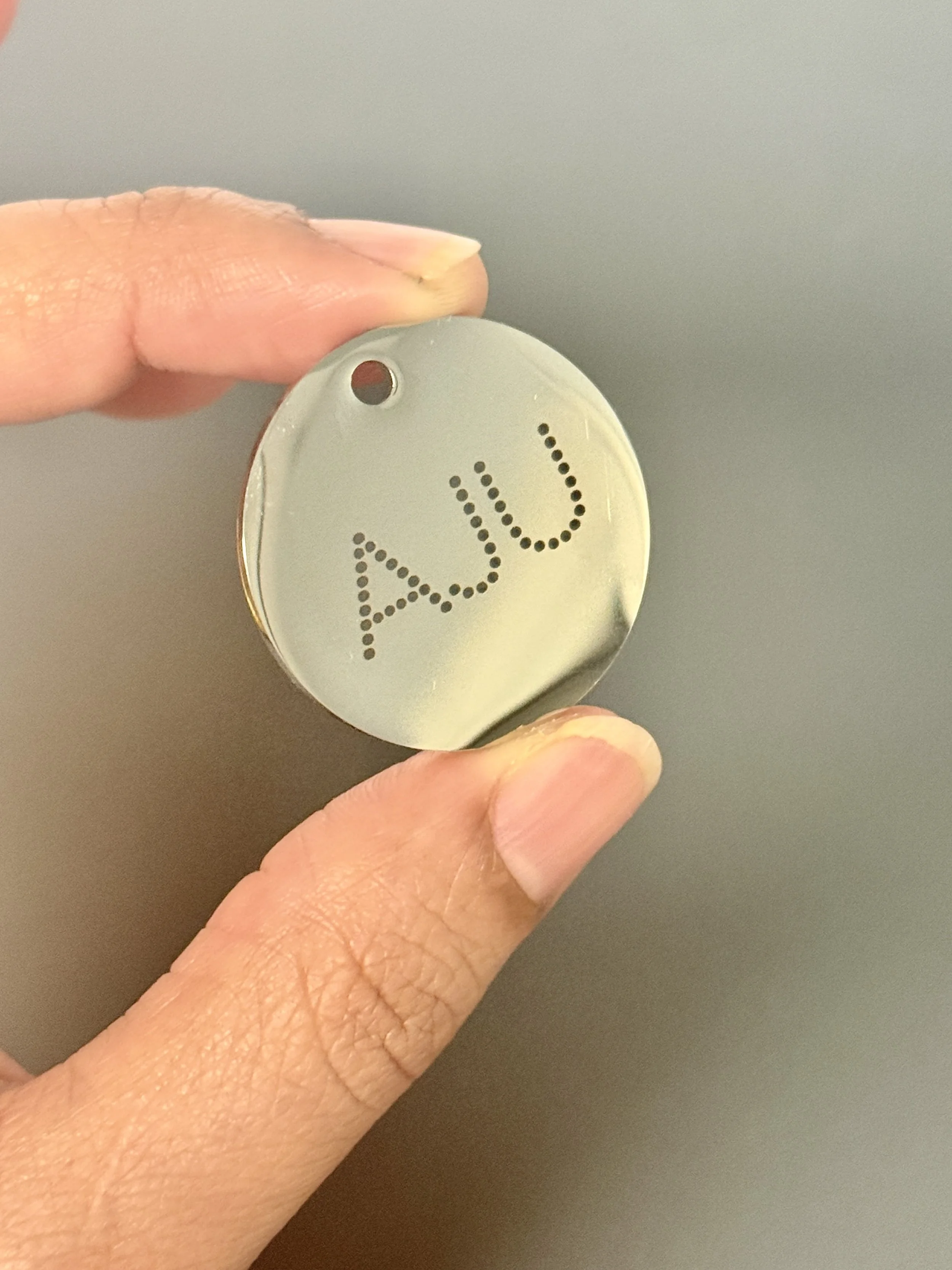Close-up of a hand holding a circular metal object with the word 'A.U.' made of small holes in the center.