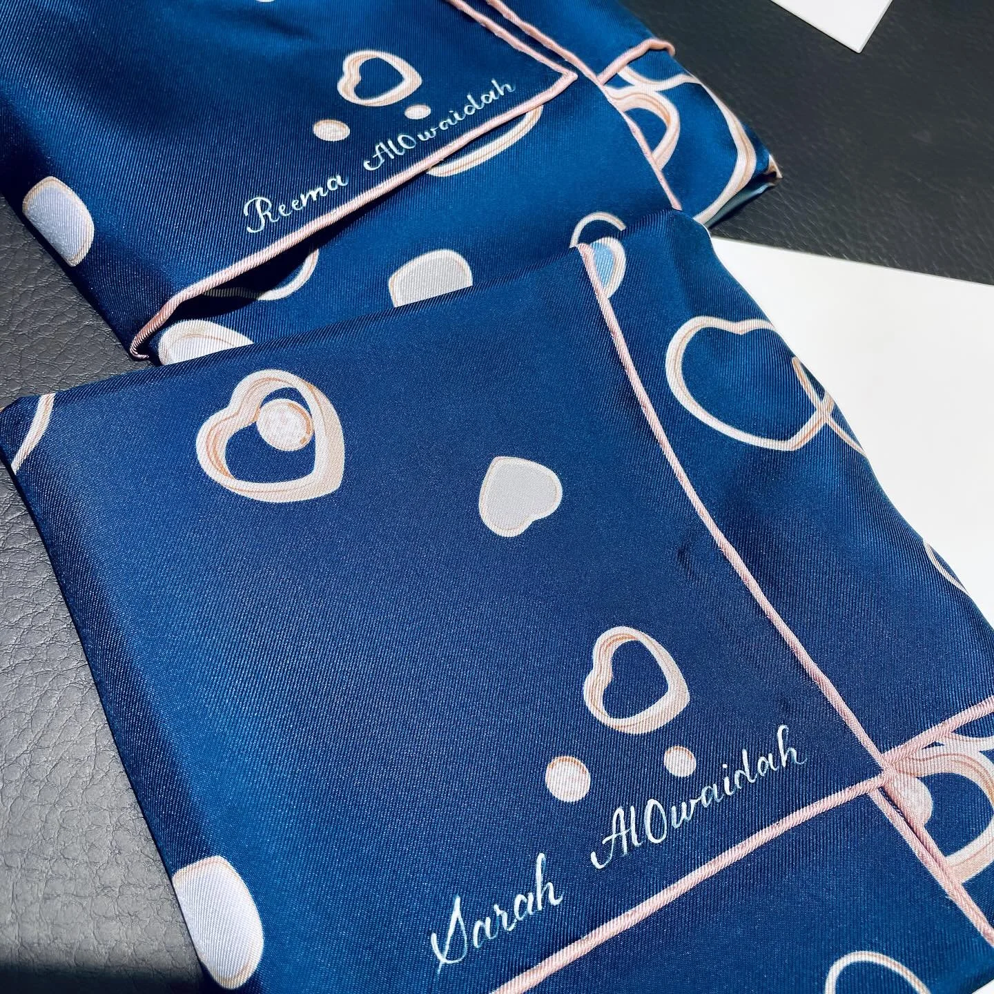 Two rolled blue gift boxes with pink ribbon and heart patterns, one with the name 'Reema Alwardah' written on it.