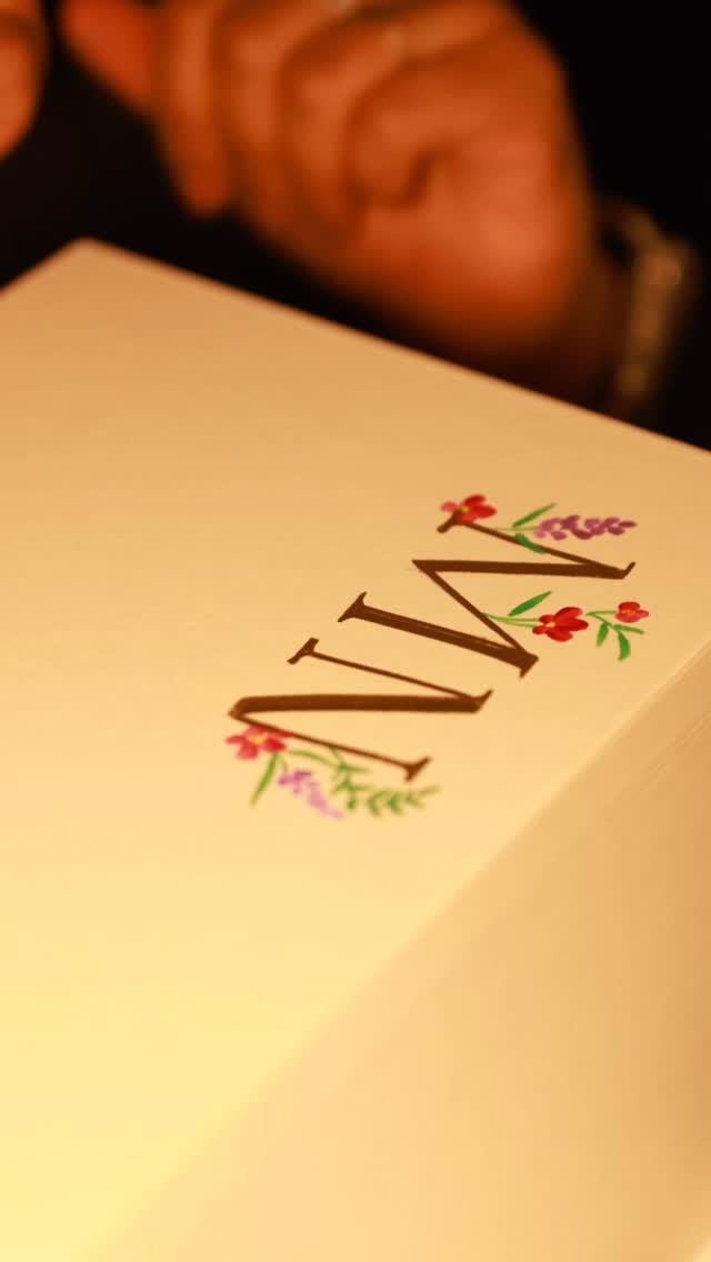 Close-up of a card with the word 'WINE' written on it, decorated with colorful flowers; a person's face is partially visible in the background.