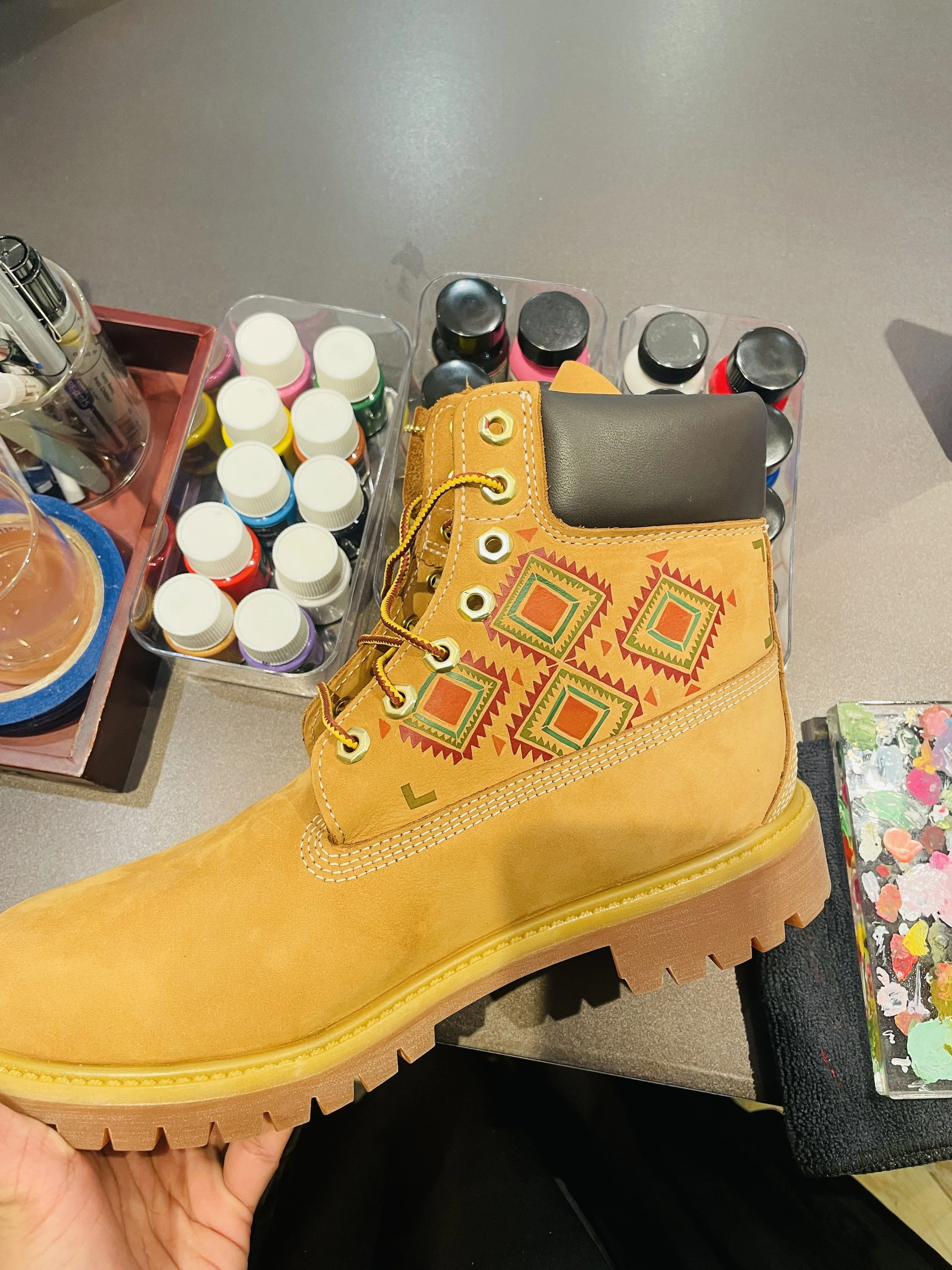 Close-up of a yellow leather boot with black, red, white, purple, and green paint bottles and a black pouch inside the boot.