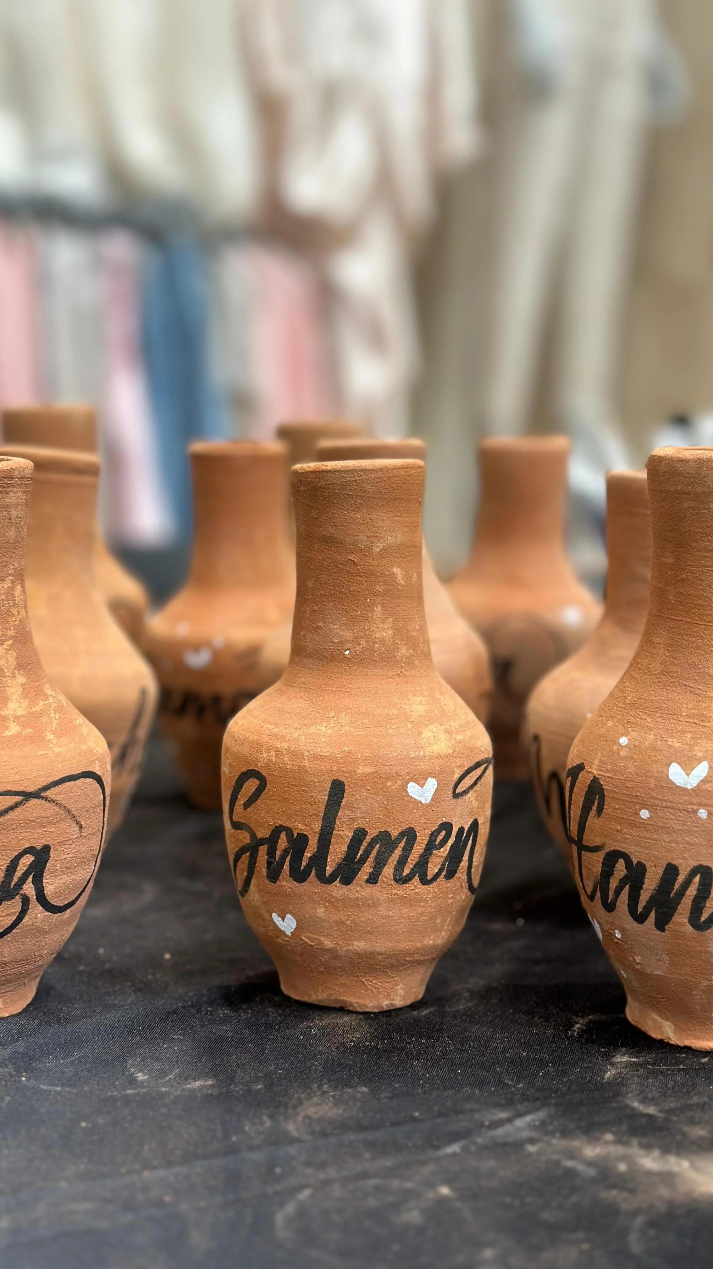 Small terracotta pots with handwritten words and small heart drawings on them, arranged on a black surface.
