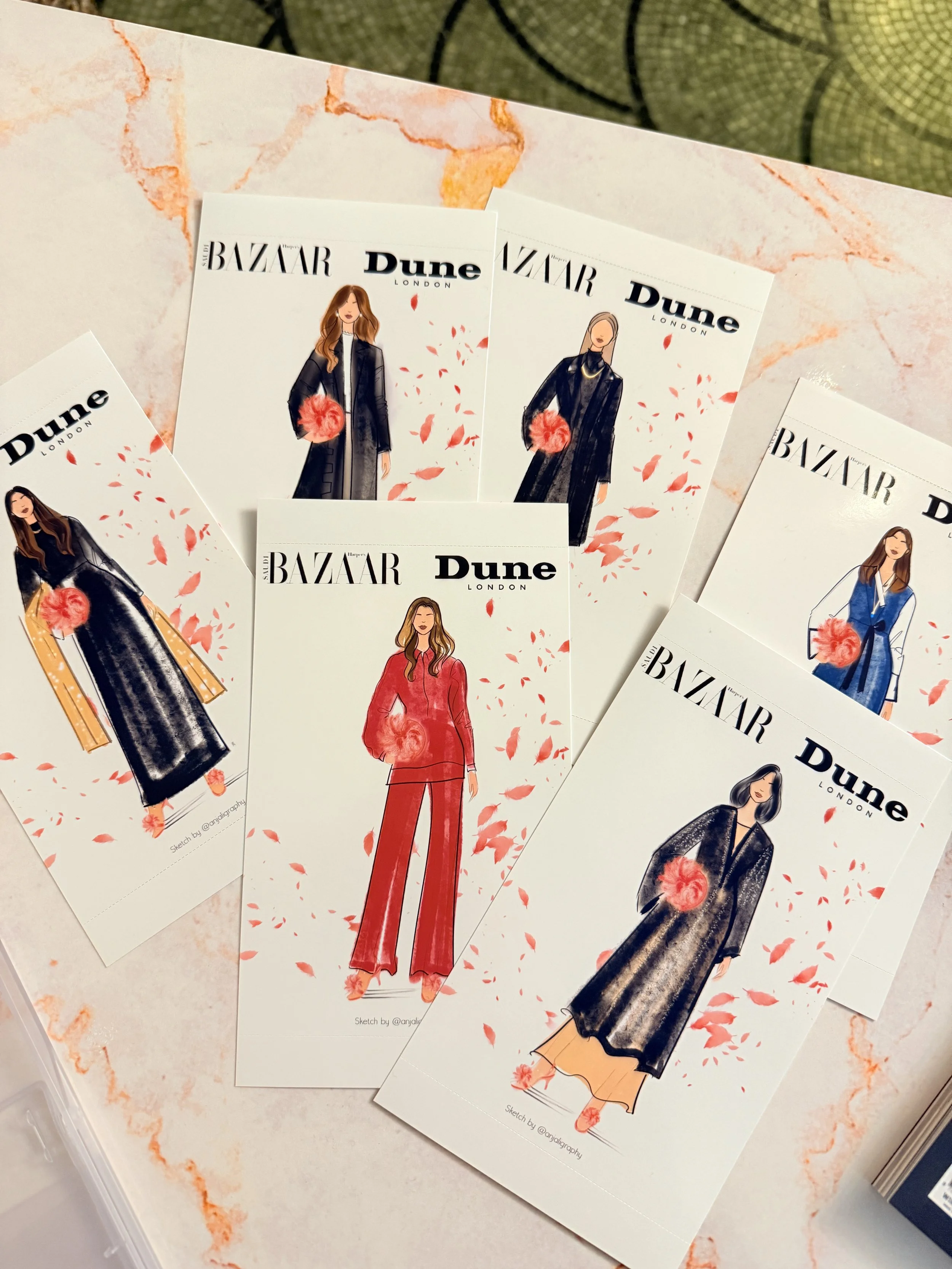 Several illustrated fashion sketches featuring women in stylish outfits, with text 'Harper's BAZAAR Dune London' on each, laid out on a pink and orange marble-patterned surface with a green decorative item in the background.