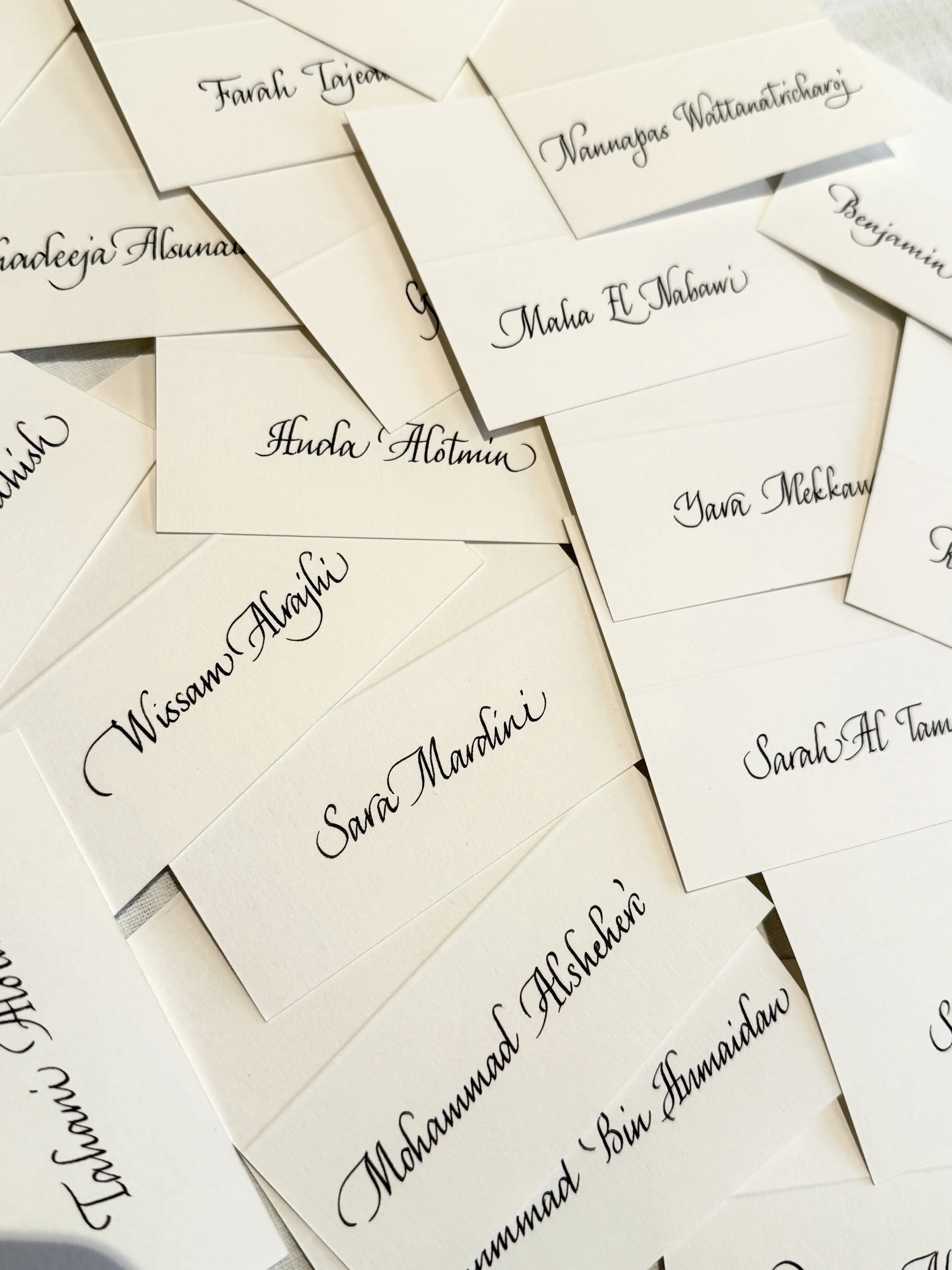 Multiple white paper cards with black cursive handwritten names scattered on a white surface.