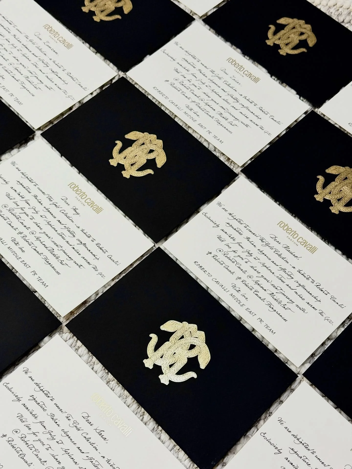 A collection of wedding or event invitations featuring black and white cards with gold and black embossed logos and handwritten text.