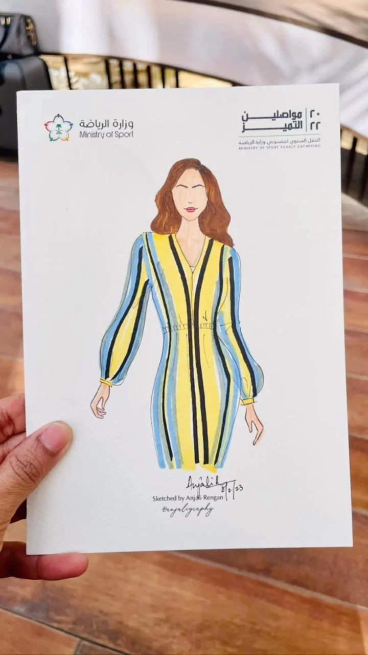 An illustration of a woman wearing a yellow dress with black, blue, and white vertical stripes, with a drawstring waist, long sleeves, and a V-neck, created by Anjali Rengan, displayed on a sheet of paper.