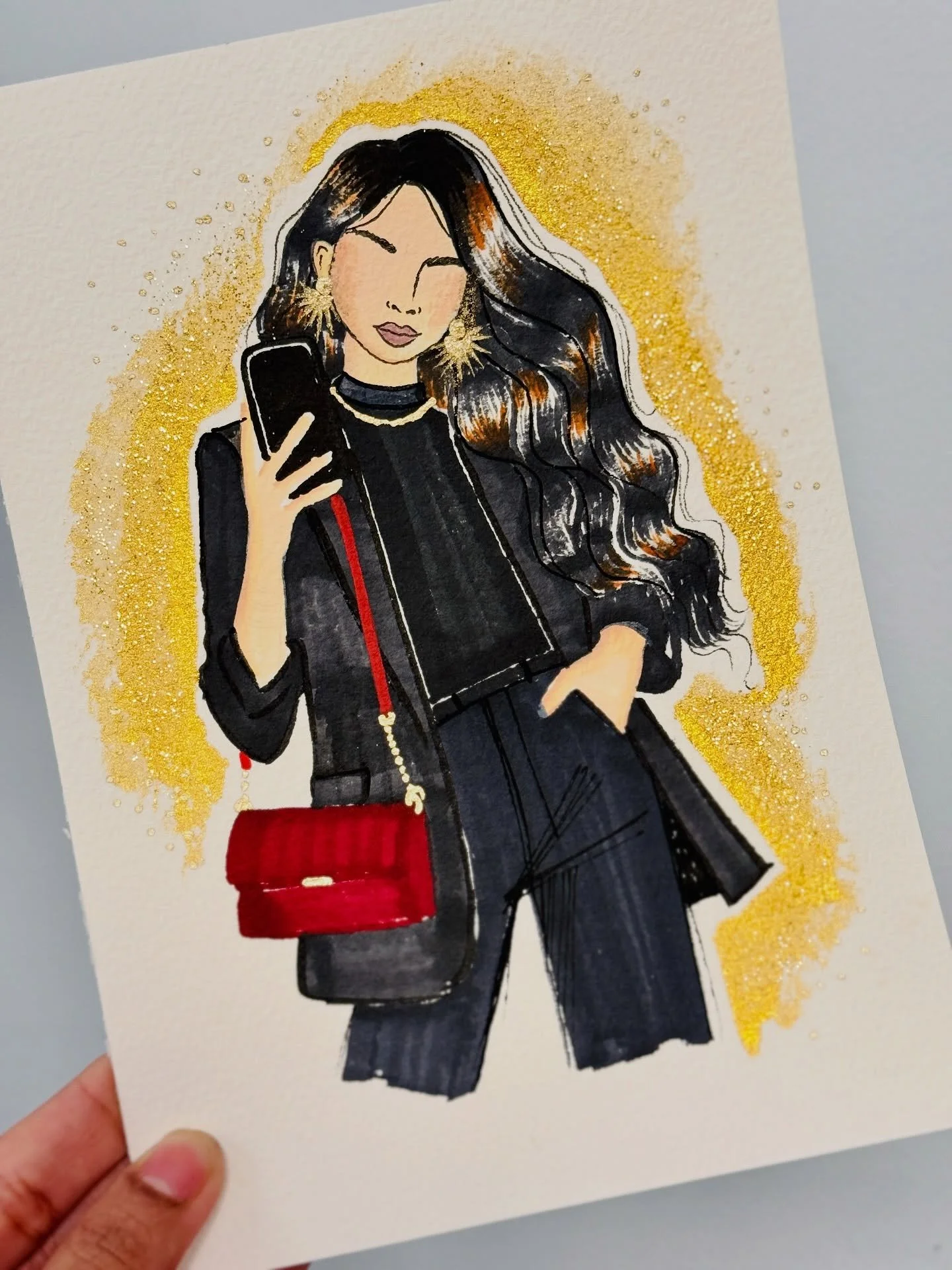 Illustration of a woman with long wavy hair, holding a phone, dressed in black with gold jewelry, gold glitter background.