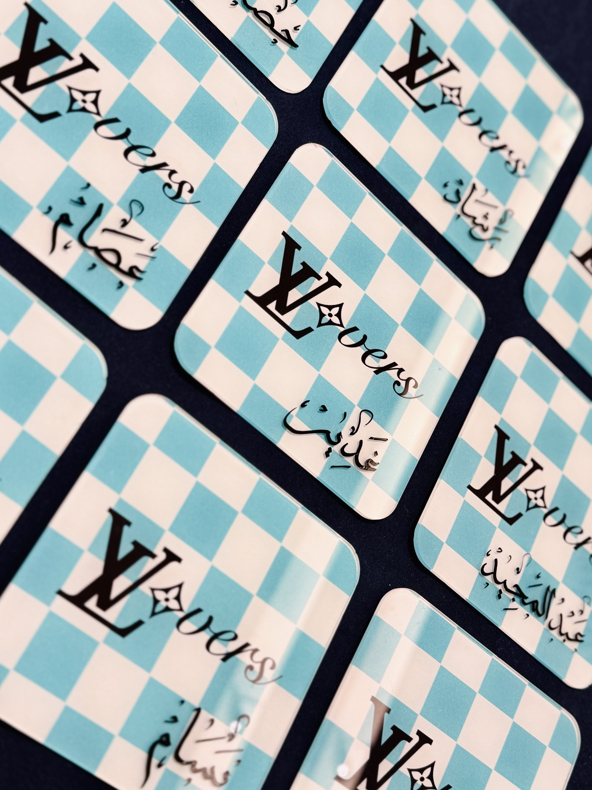 Close-up of several blue and white checkered playing cards with the word 'Louis' and a logo, fanned out on a dark surface.