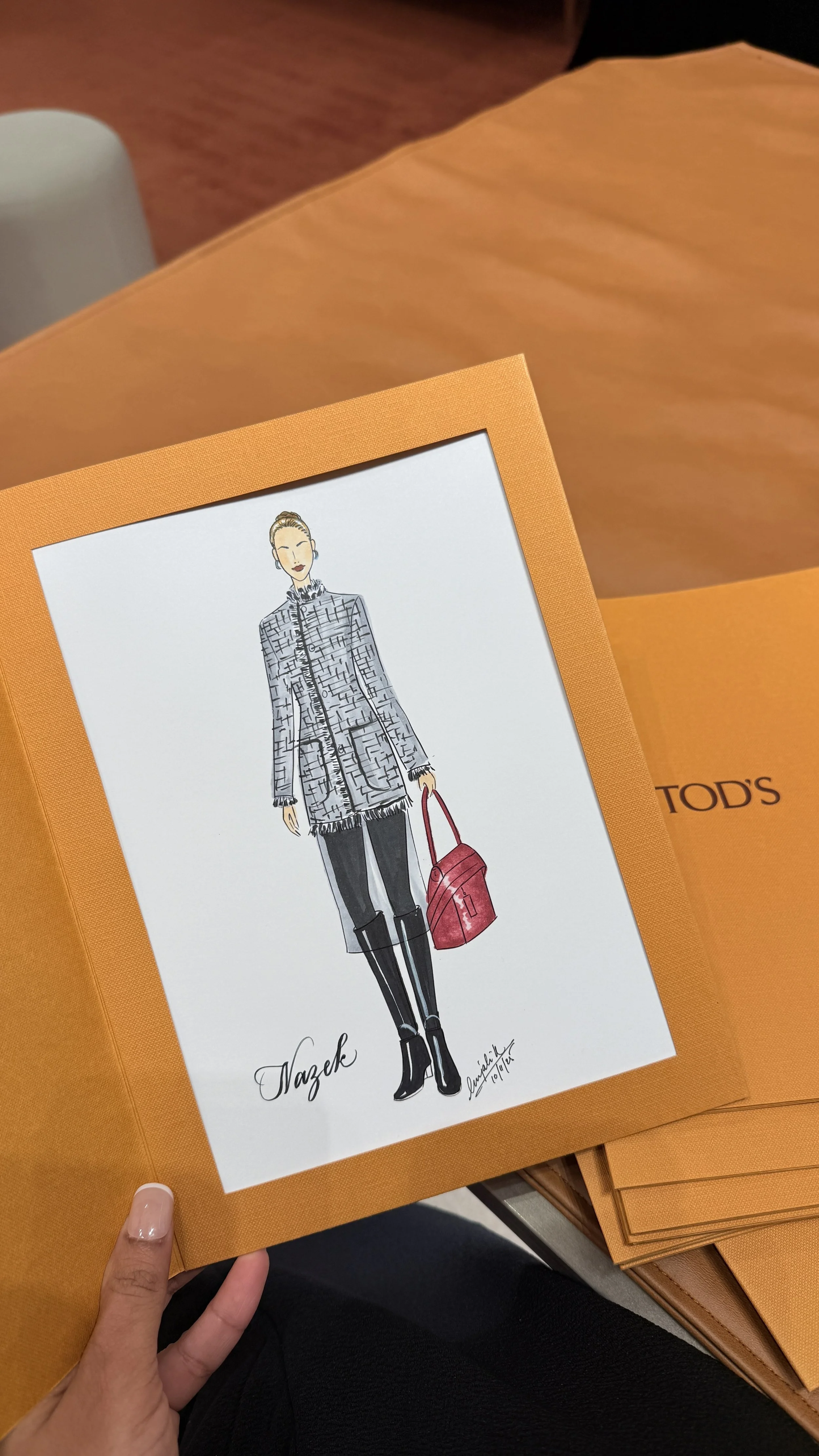 Fashion sketch of a woman in a plaid coat, black leggings, and high boots, holding a red handbag, framed in orange.