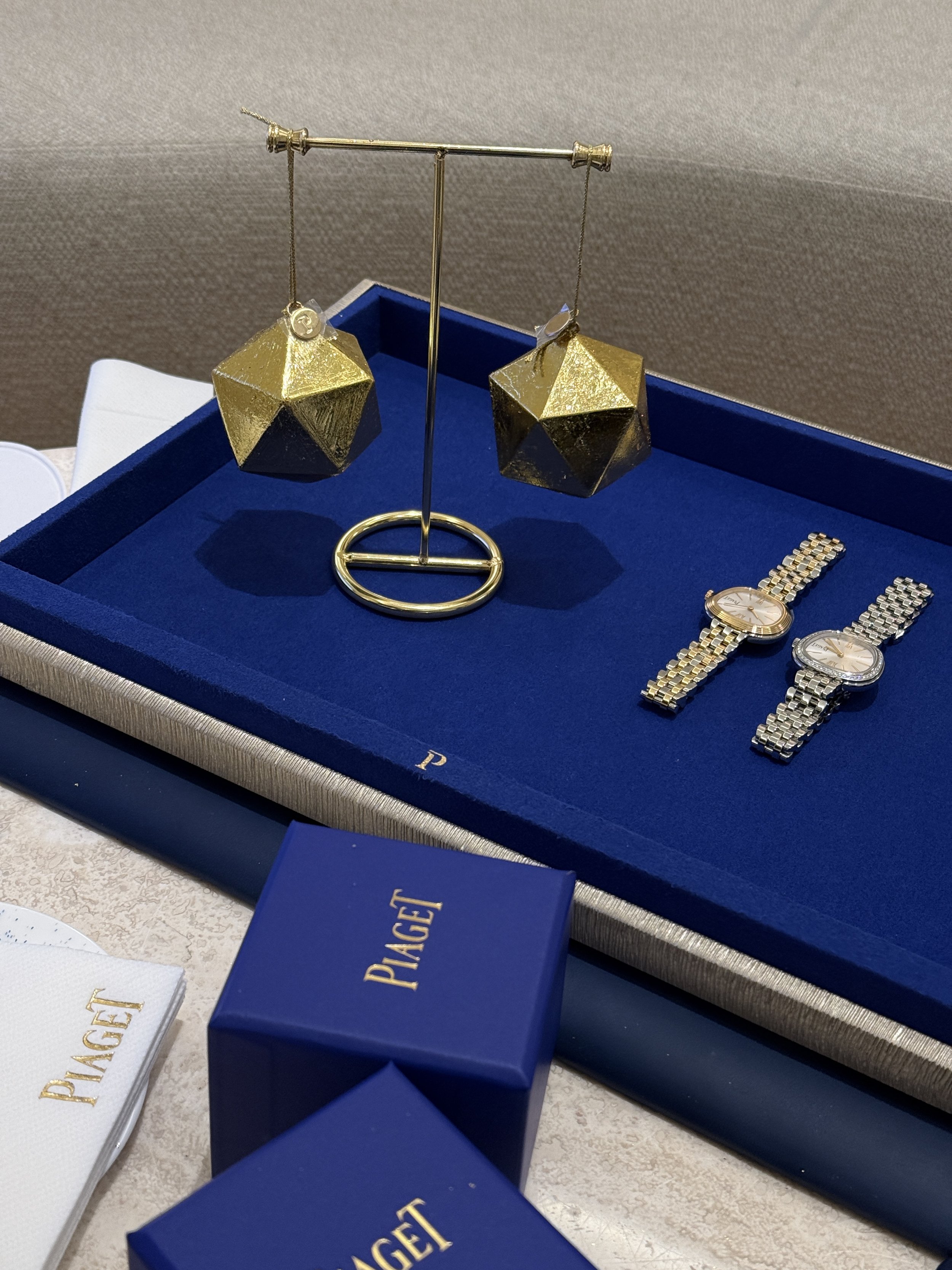 A display of gold and silver watches and gold geometric earrings with a blue and white jewelry box in the background, inside a boutique or jewelry store.