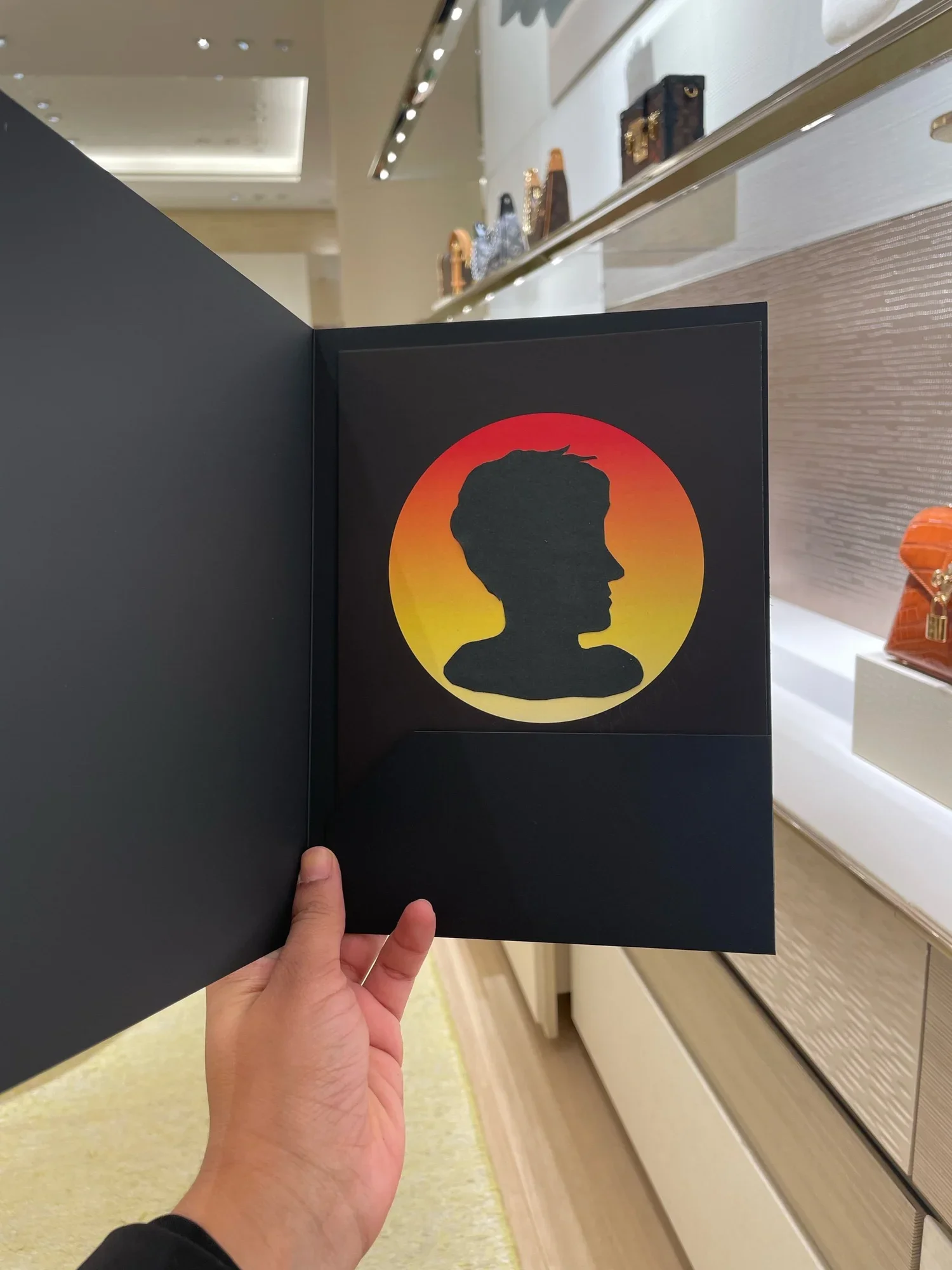 A person holding open a black book or folder with a silhouette of a person’s profile on a red and yellow gradient background inside.