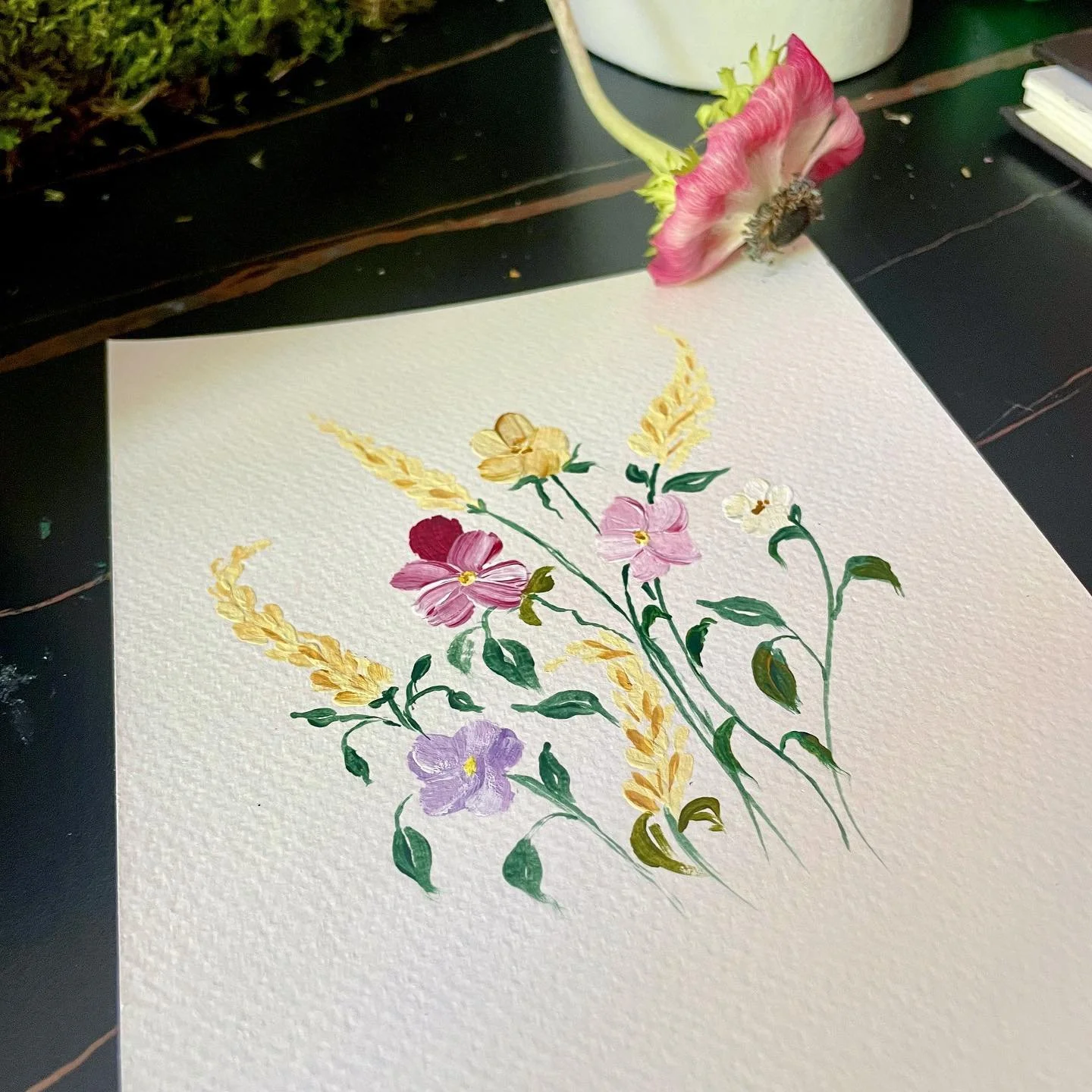 Hand-painted watercolor floral illustration featuring pink, purple, and yellow flowers with green leaves on textured paper.