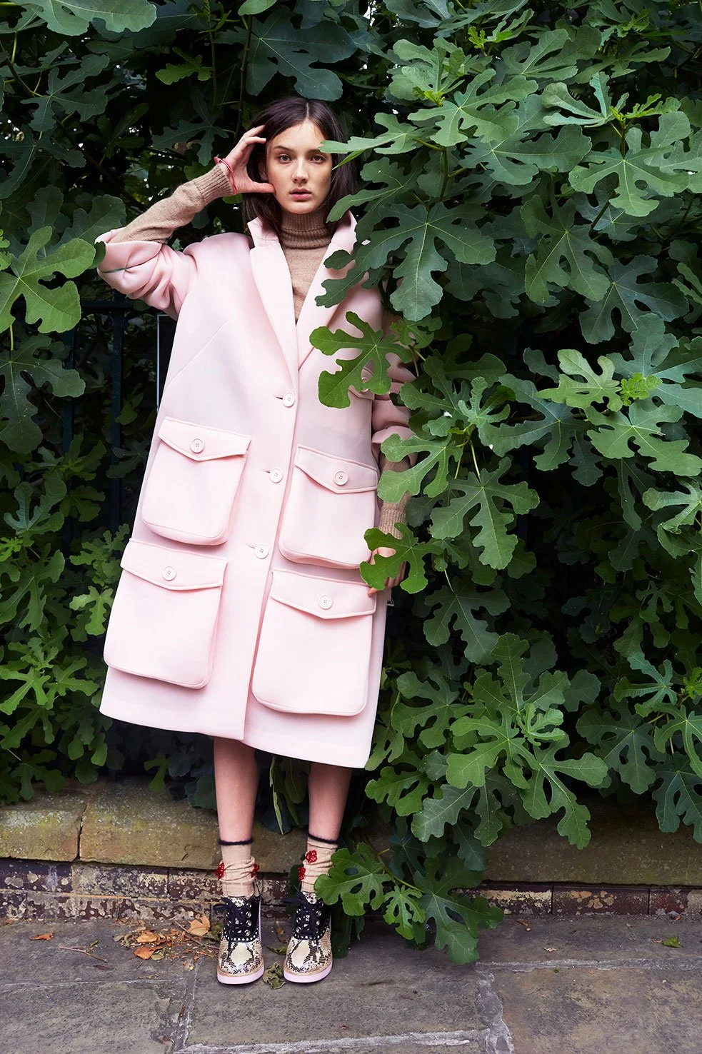 Model in a pale pink oversized coat against lush green foliage, styled by Zoe James for Flair.