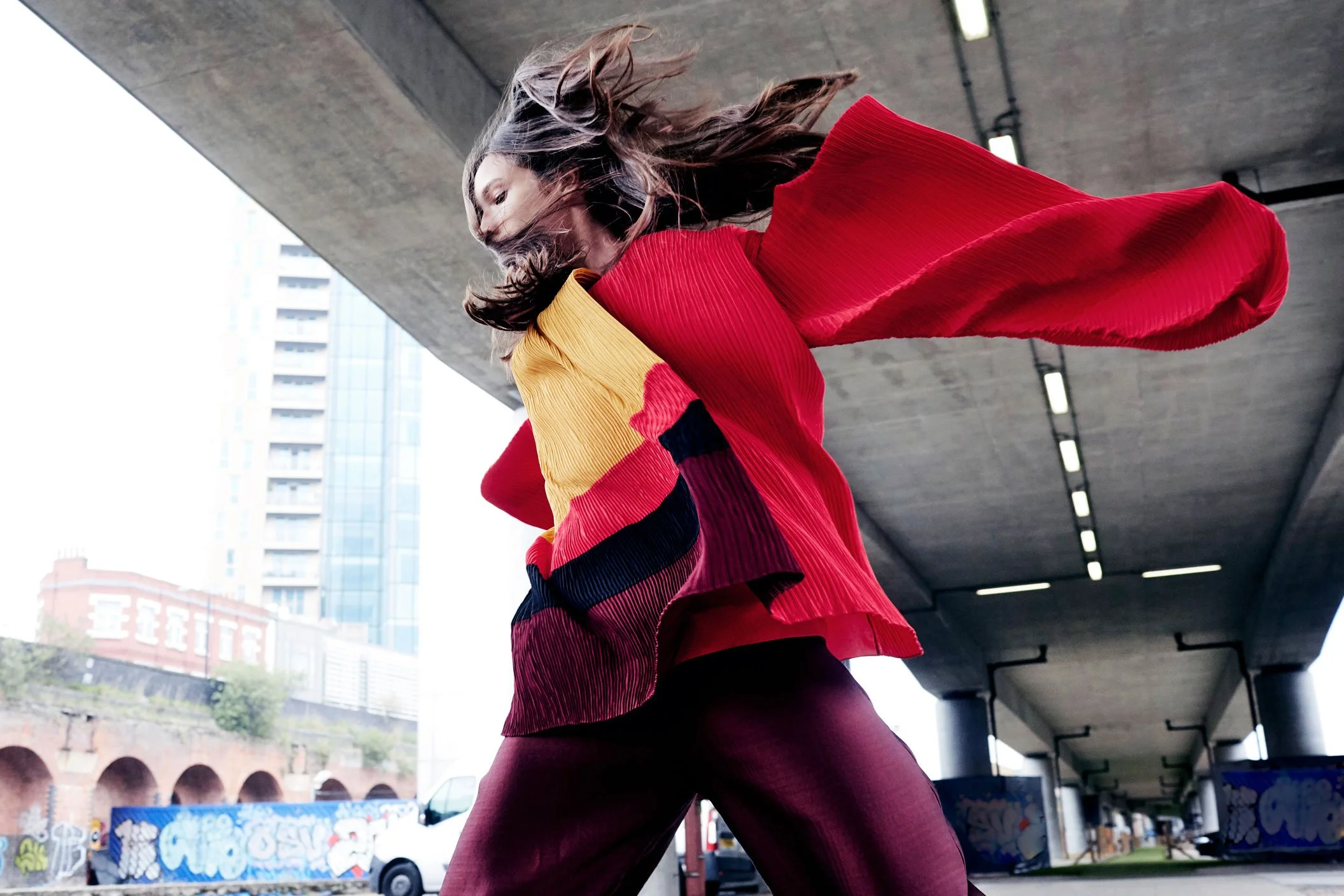 Dynamic shot of a model in a red, yellow, and burgundy outfit, emphasising movement and texture.