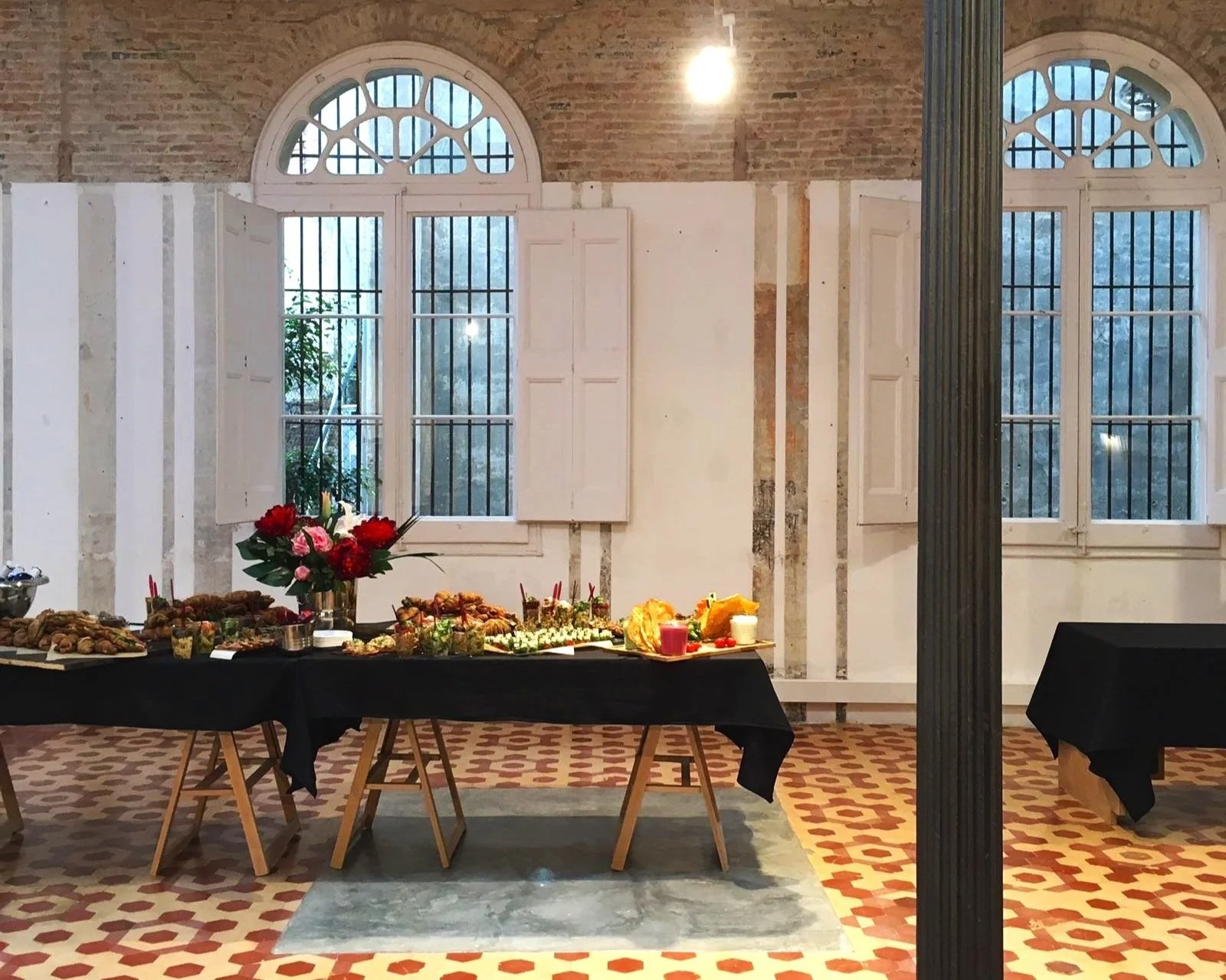 Indoor buffet with assorted foods and a red flower centerpiece, set against brick walls and large windows