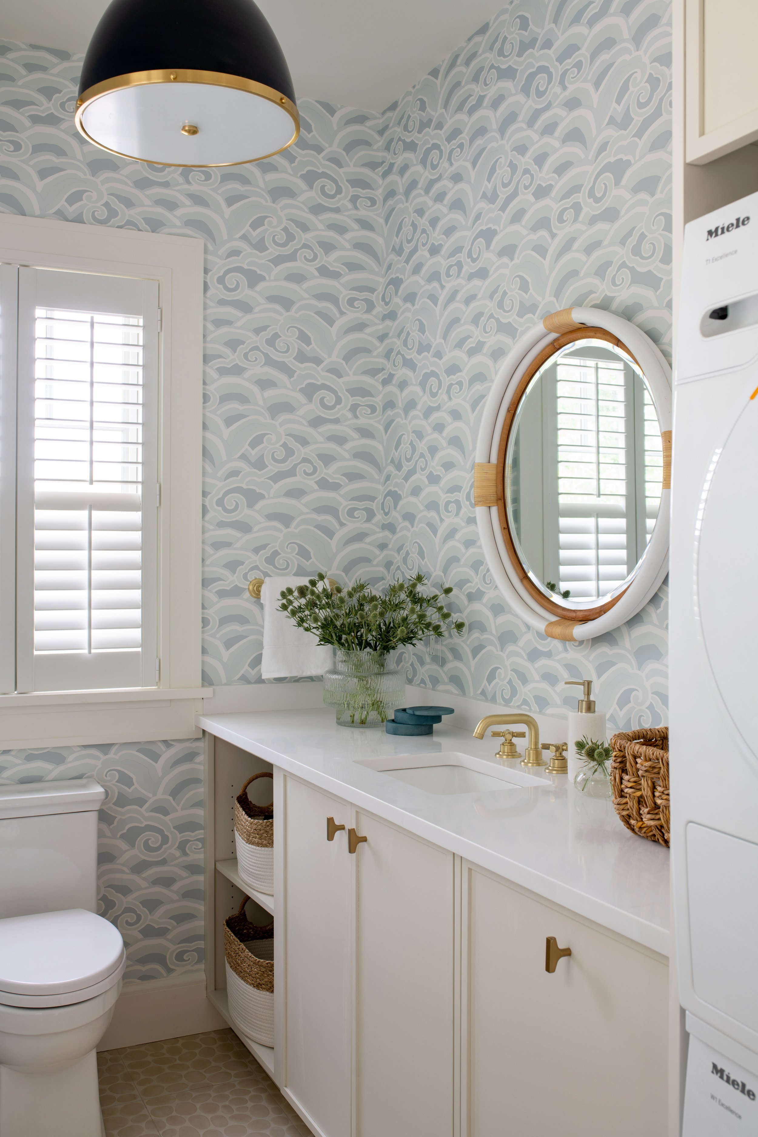 Coastal white powder room with soft blue wallpaper and brass accents.