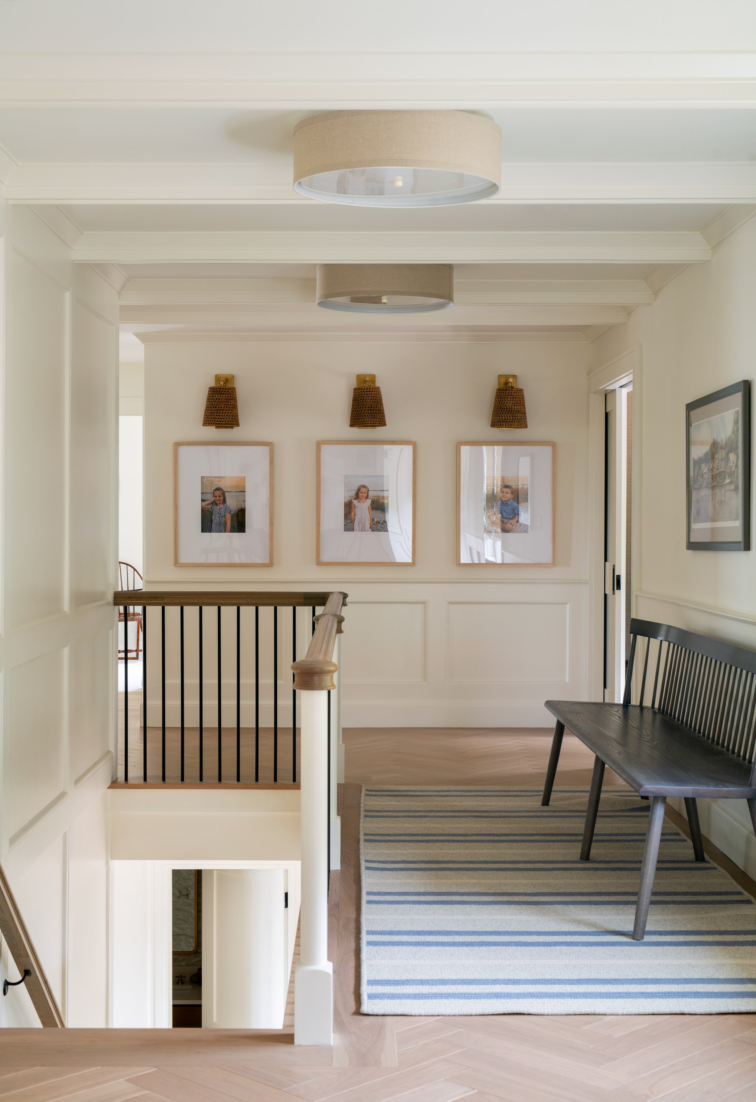Hallway runner leading to family photos that are accented with textured coastal wall sconces which act as picture lights in this bright, airy, coastal home.