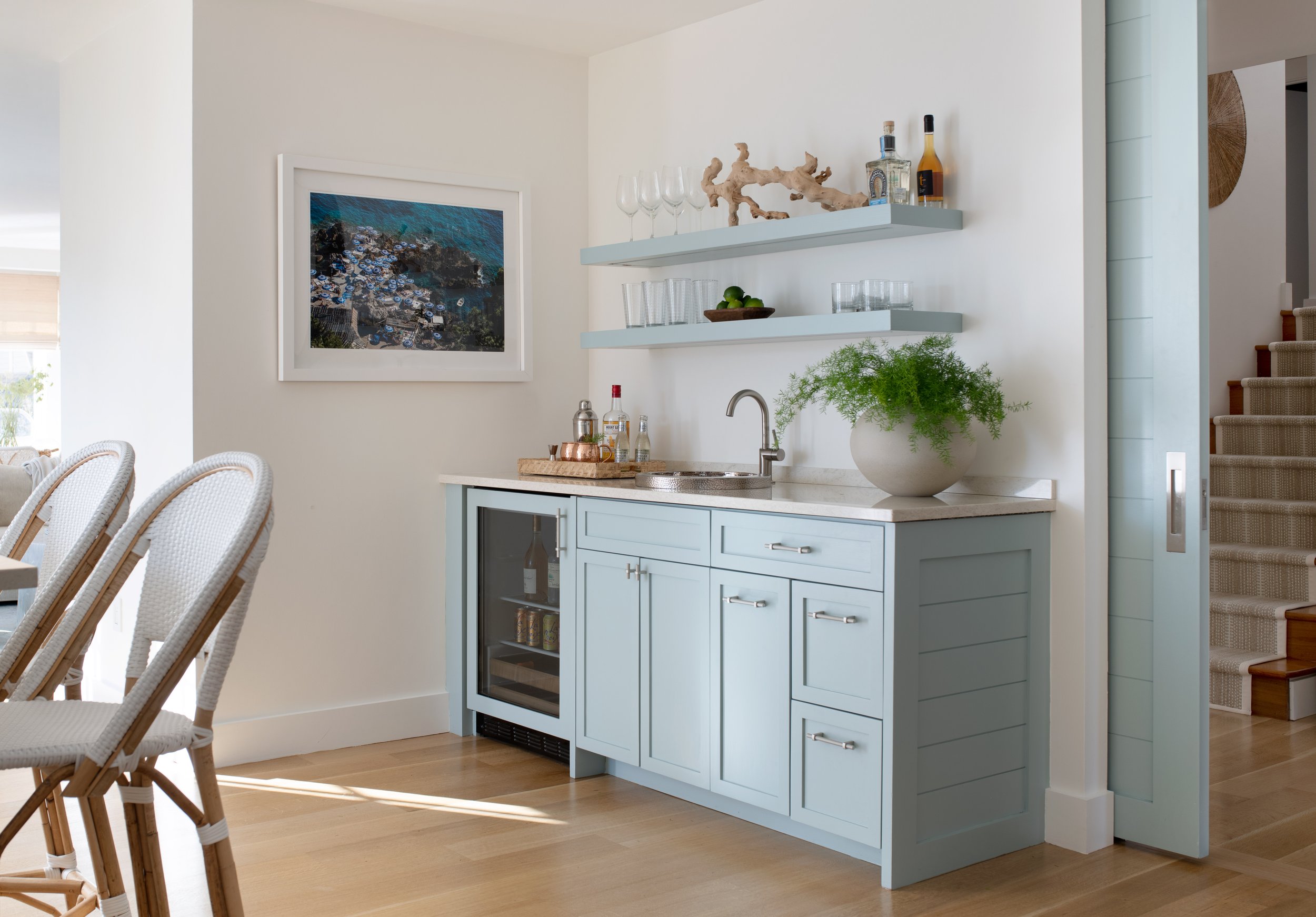 Coastal wet-bar with floating blue shelves, a beverage fridge, and nickel accents. Blue pocket door with accent cabinetry. Open concept kitchen with a wet bar.