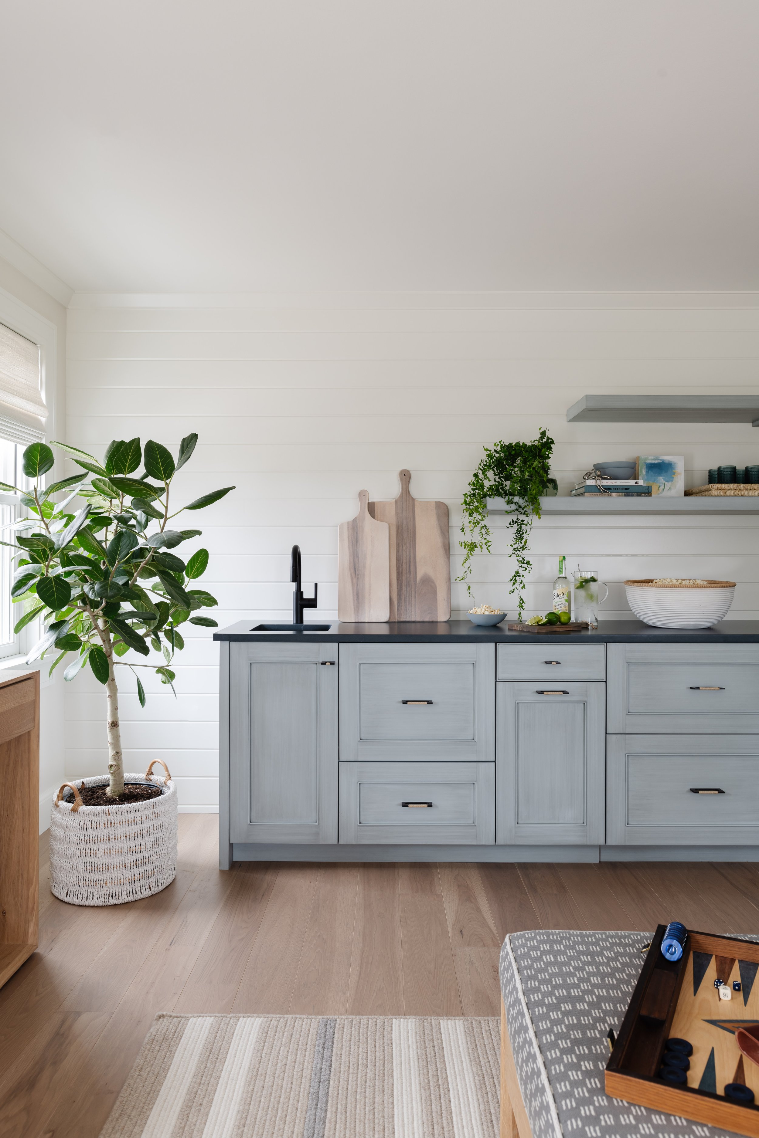 Sitting room with a wet-bar! Coastal, blue cabinetry, with a black countertop, bronze hardware, and wood-planked walls.
