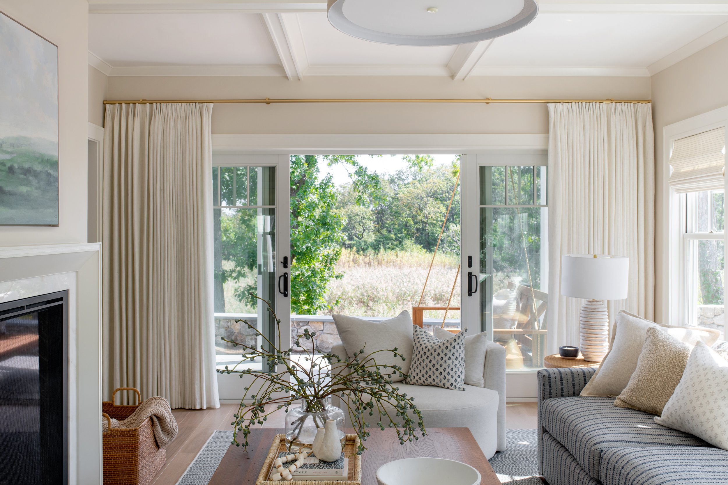 A sitting room with a view! Overlooking the water and some stunning marsh-land, this coastal sitting room has one large sofa, two oversized swivel chairs, and white drapery with brass accents.