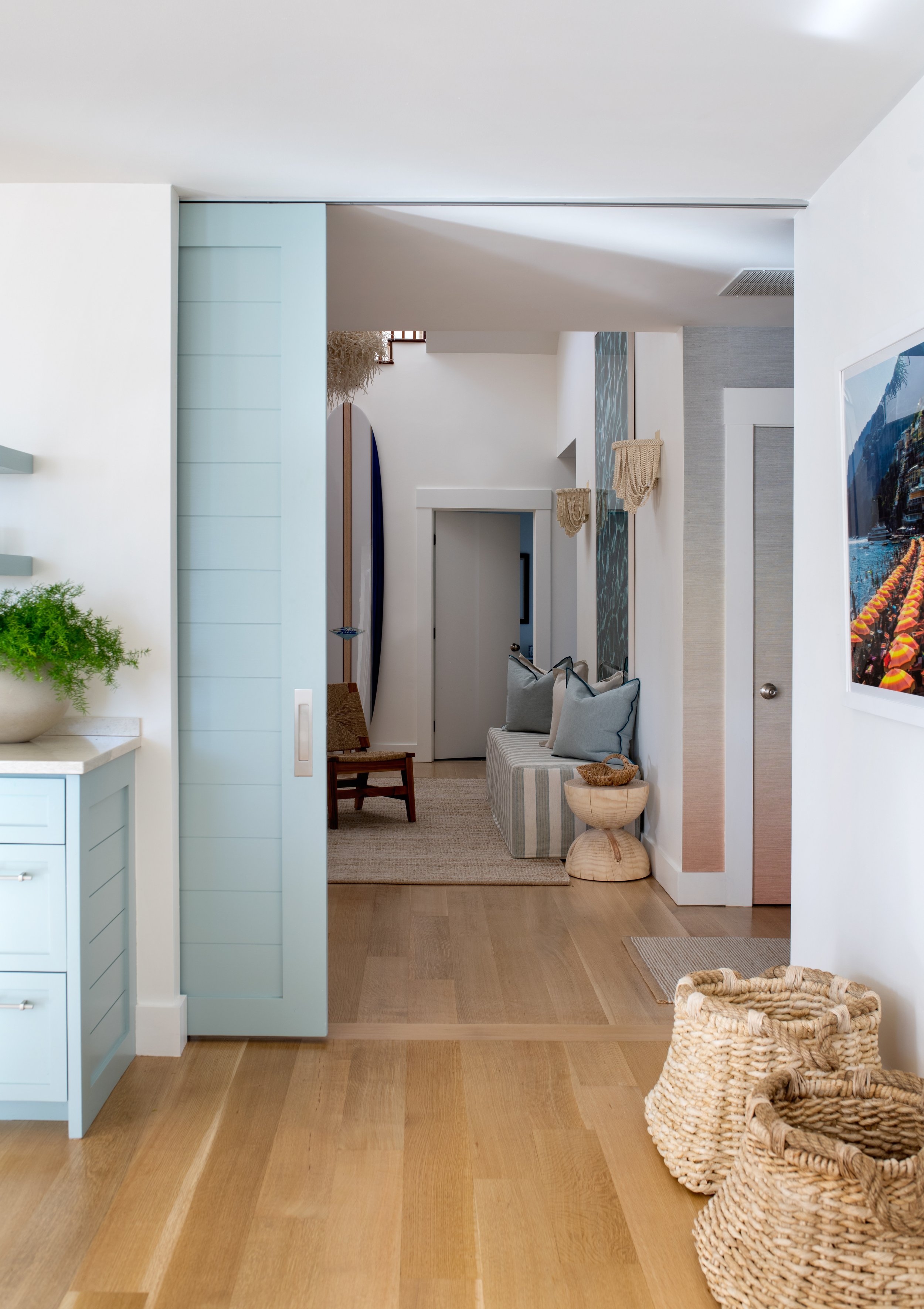 Coastal home with a blue pocket door and woven accents. Bright airy coastal home with blue accents and white walls.