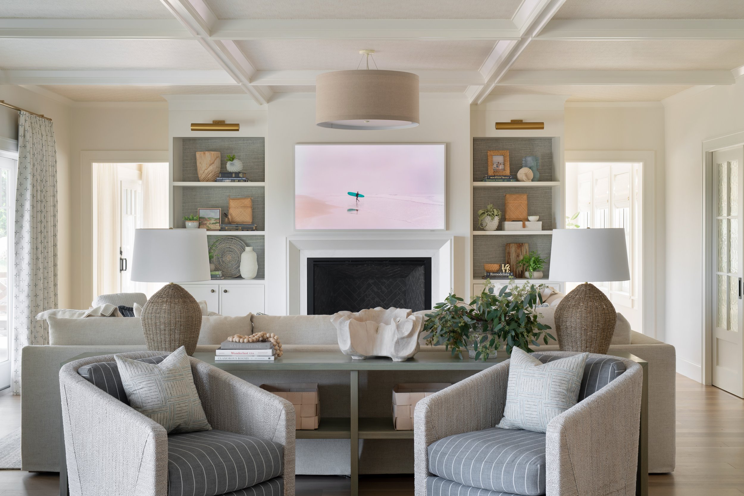 Coastal living room with swivel chairs, a contrasting console table, and built-in bookshelves backed with wallpaper.