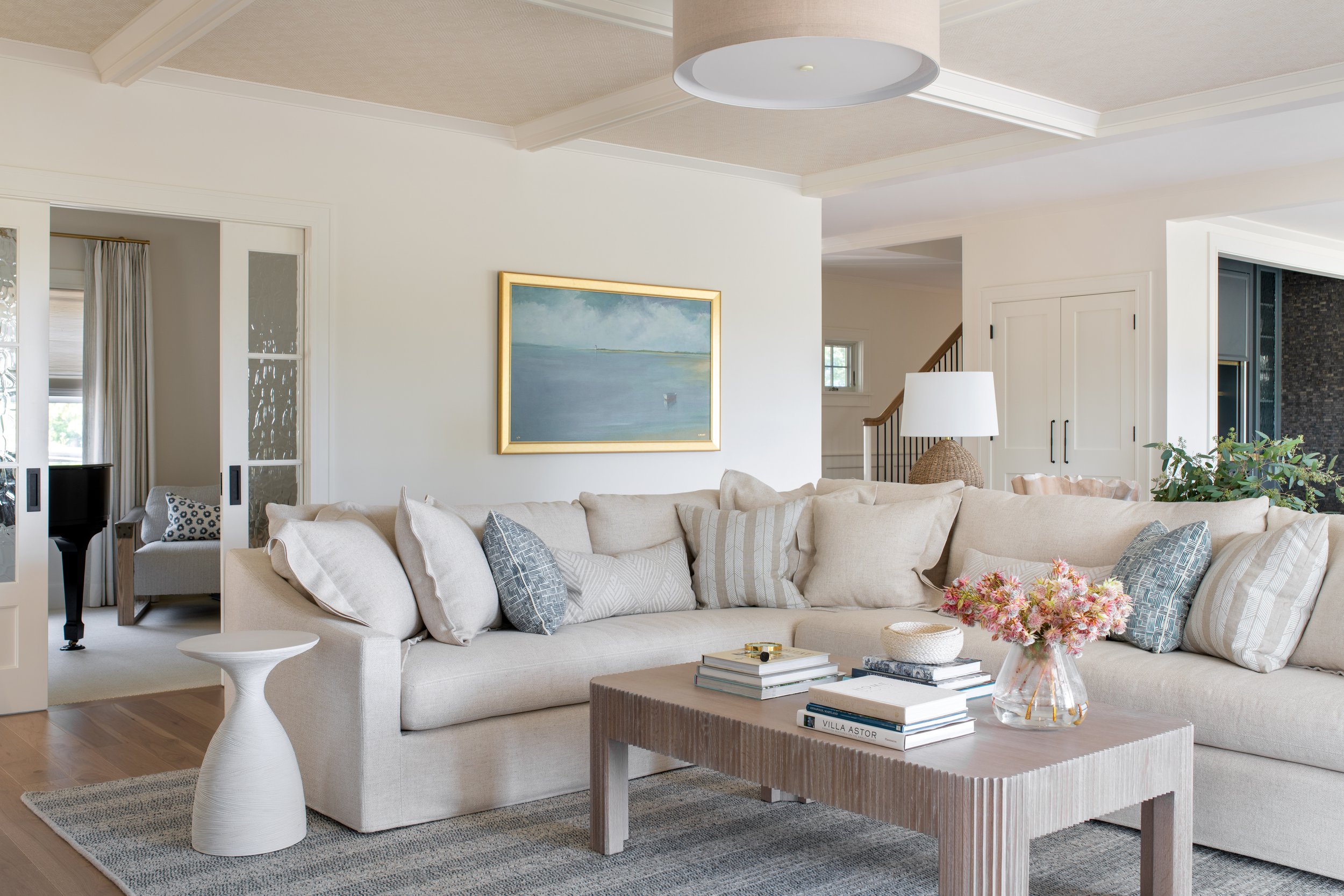 Coastal living room with a large sectional, textured coffee table, and wallpapered ceilings. Neutral design scheme. Coastal Design.