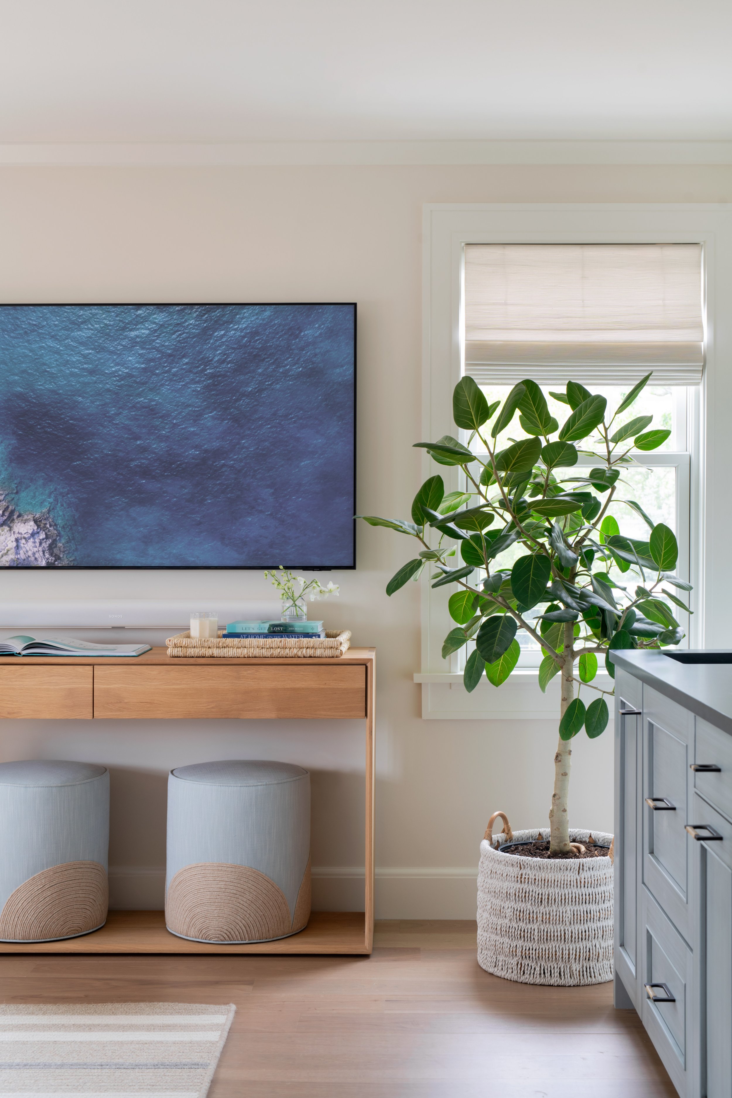 Sitting room with light-blue coastal cabinetry, upholstered ottomans with textured bases, and a simple, natural wood coffee table.