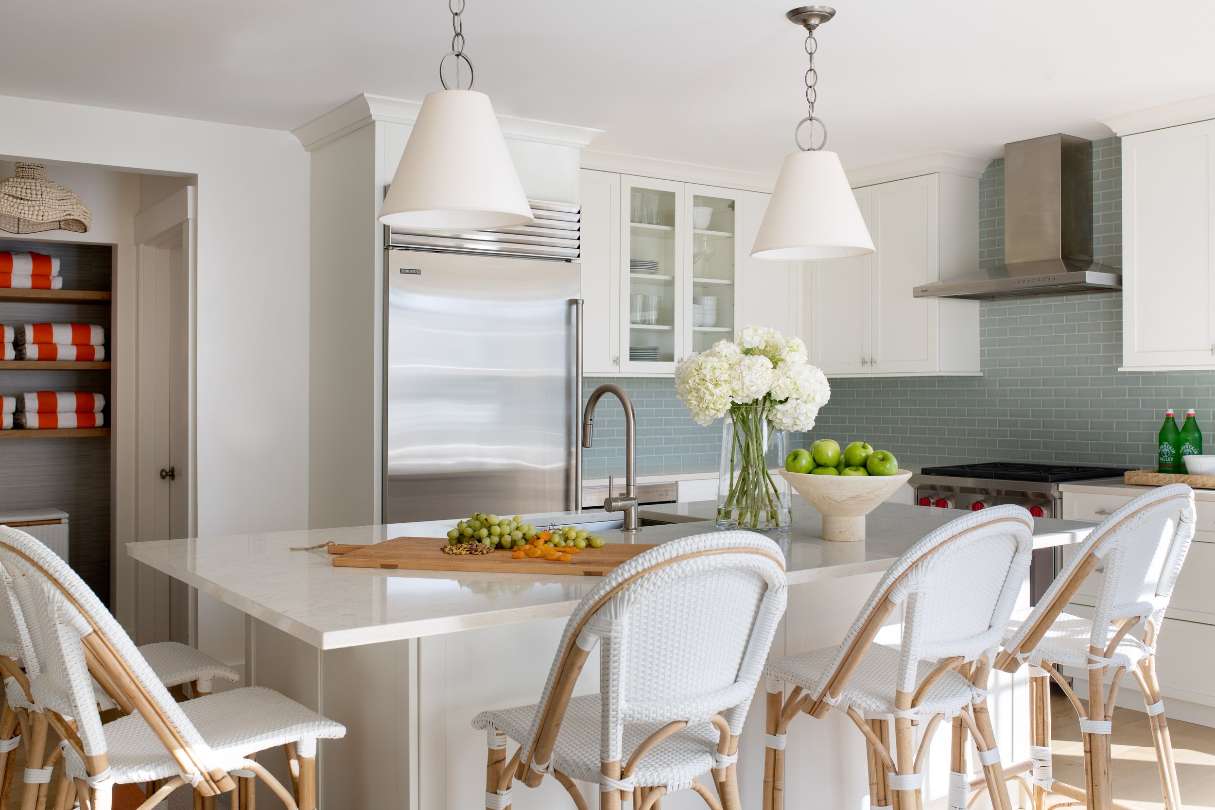 Coastal kitchen with a large White Island, blue backsplash, and with white and wood bistro-style bar stools. Barstools with backs. Washable barstools. Washable counter stools. Coastal kitchen island seating. Coastal kitchen island lighting.
