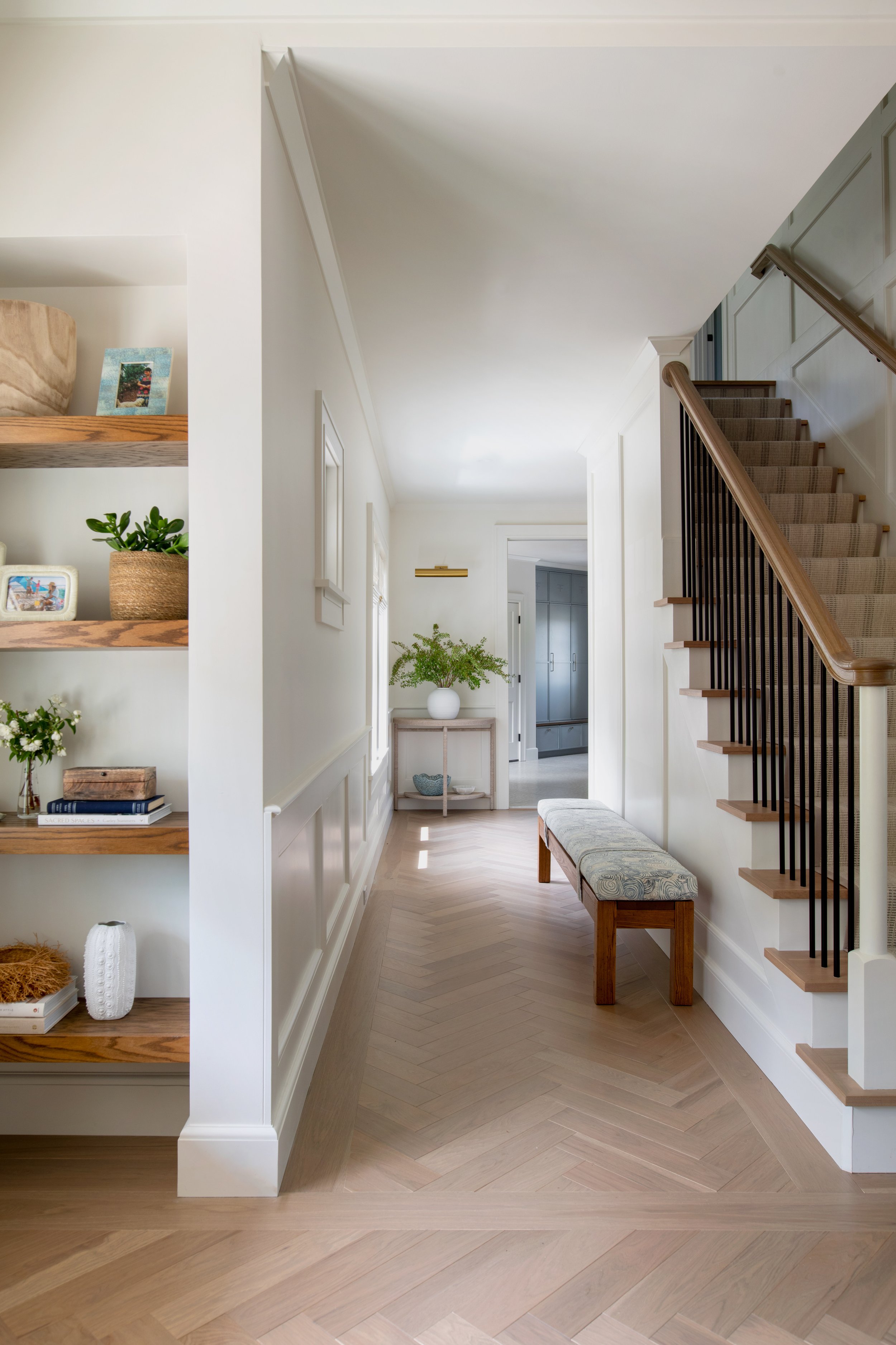 Coastal style entry hallway with built-in shelving, and a herringbone wide-plank flooring. Accent bench and table with a picture light.