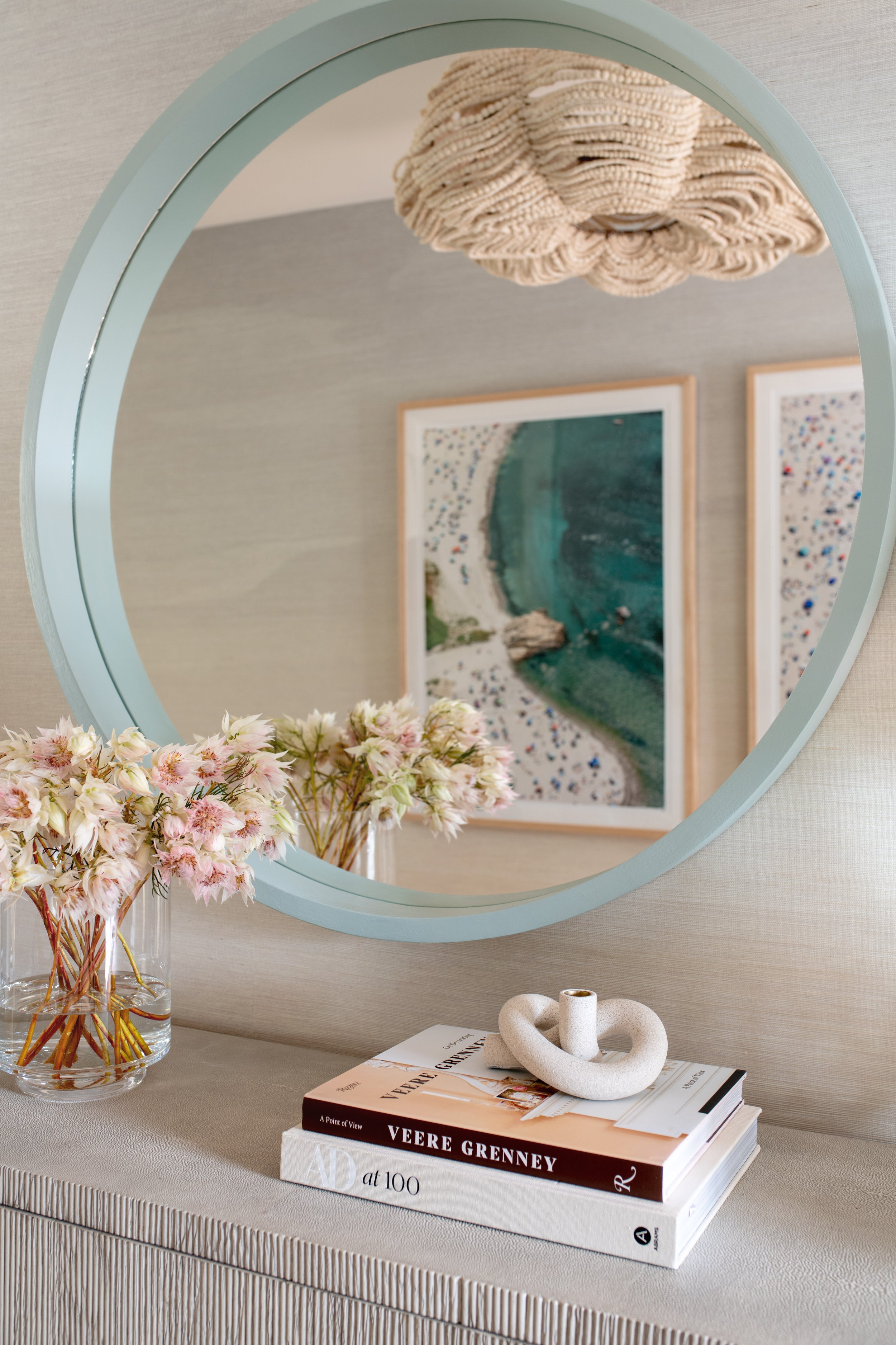 Coastal living room with textured wallpaper, beaded lighting, and blue accents. Living room accent table decor. Console table styling. Coastal accent table.