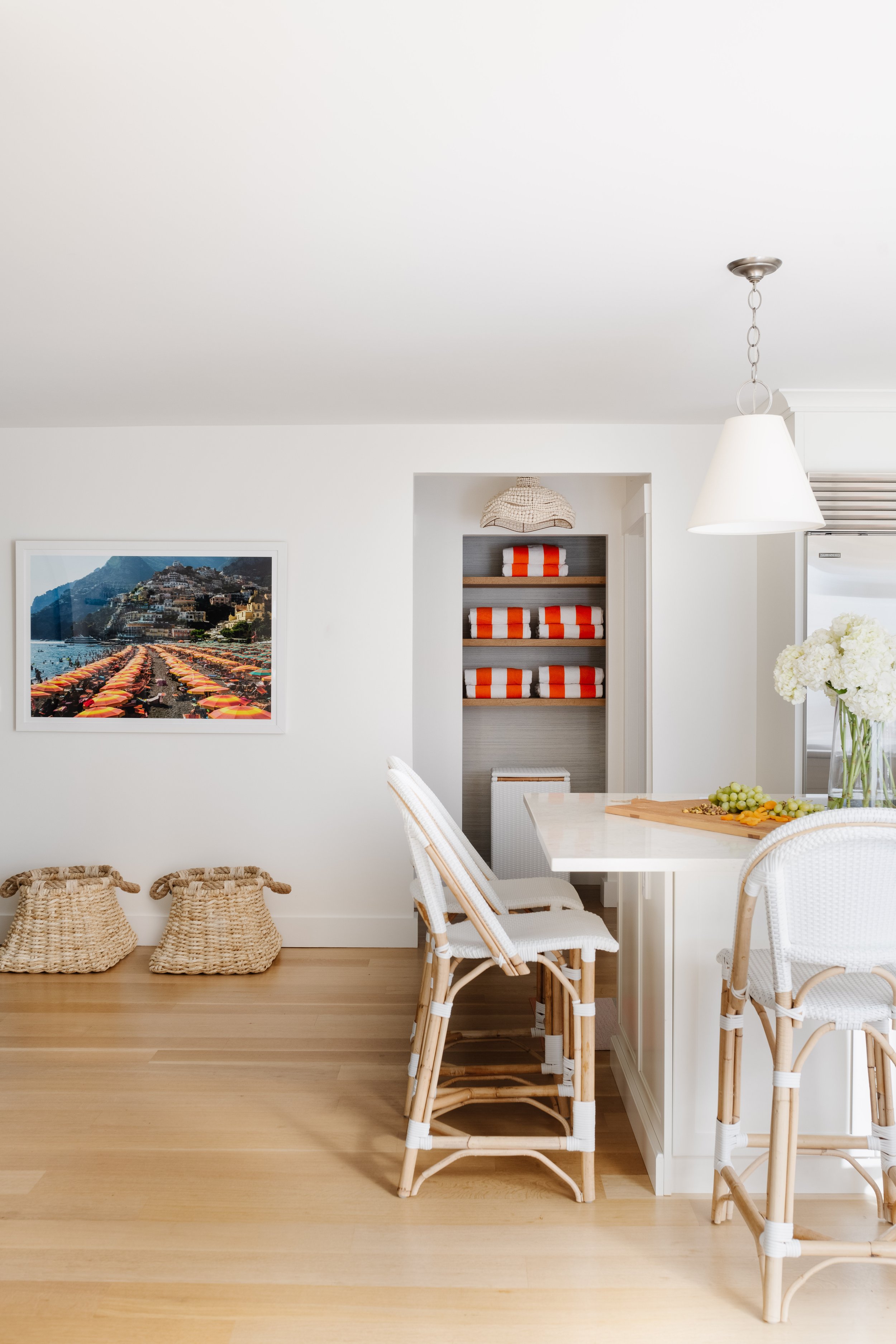 Open concept coastal kitchen with white barstools, white accent lighting, and a large kitchen island. Small storage closet in an open concept coastal kitchen.