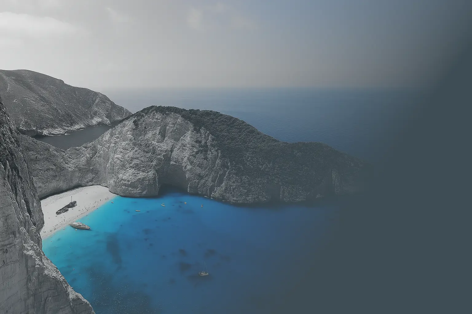 Scenic view of a coastal landscape with steep rocky cliffs, a small beach with boats, and bright blue water surrounded by misty, overcast sky. Zakynthos Shipwreck