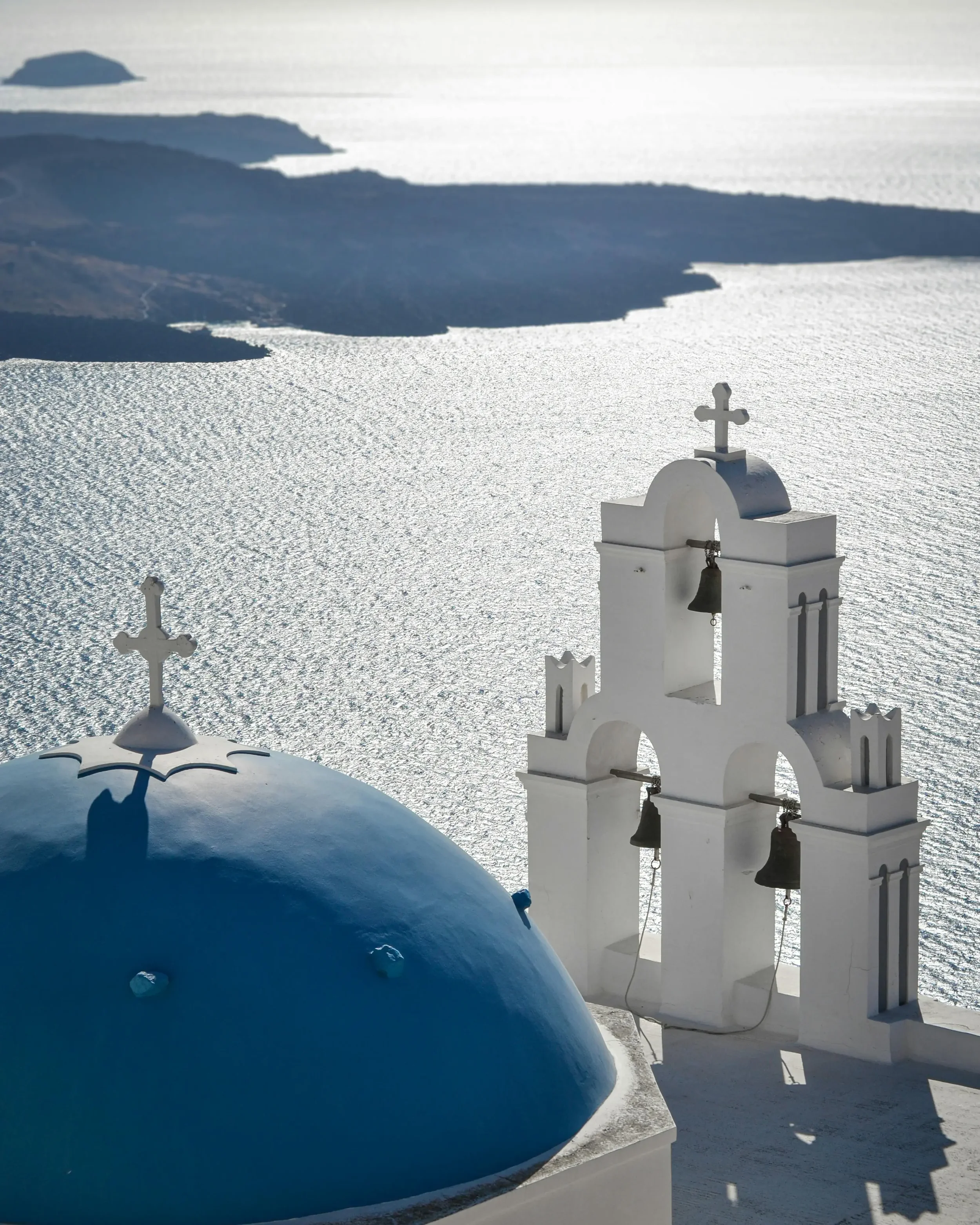 White church with blue dome and bell tower, overlooking the sea on a sunny day.