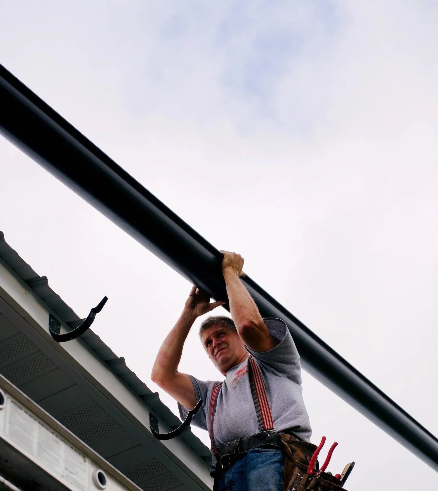 Installing a black half-round gutter on the side of a building.